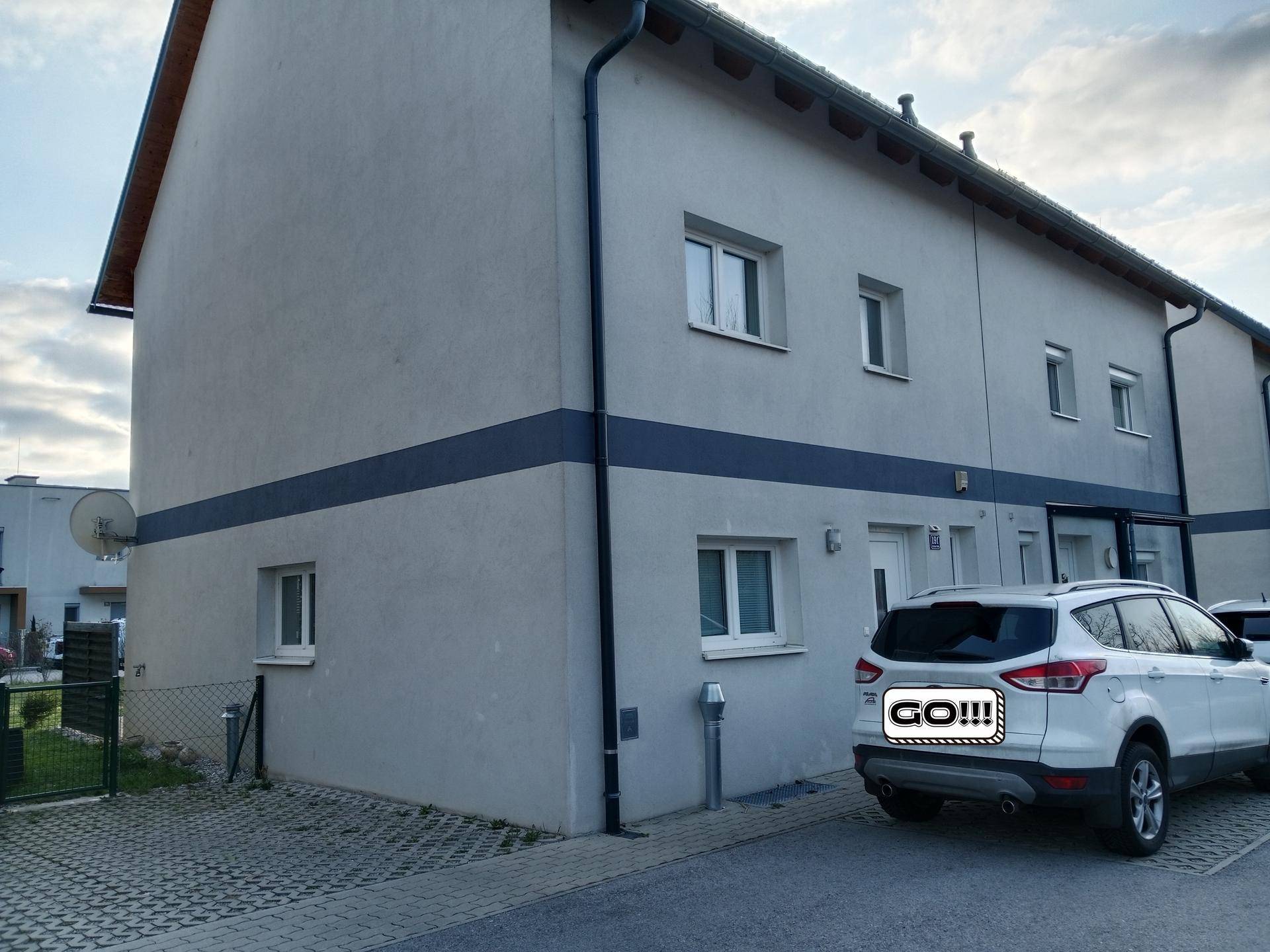 Moderne Reihenhausfassade mit Parkplatz und blauen Akzentstreifen.