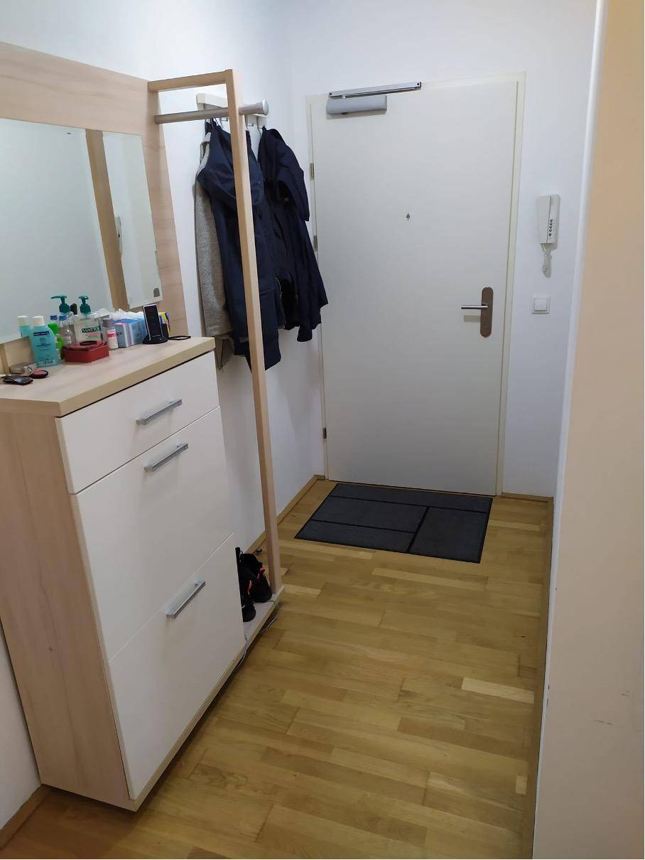 Heller Eingangsbereich mit Garderobe, Spiegel und Holzfußboden, führt zur Wohnungstür.
