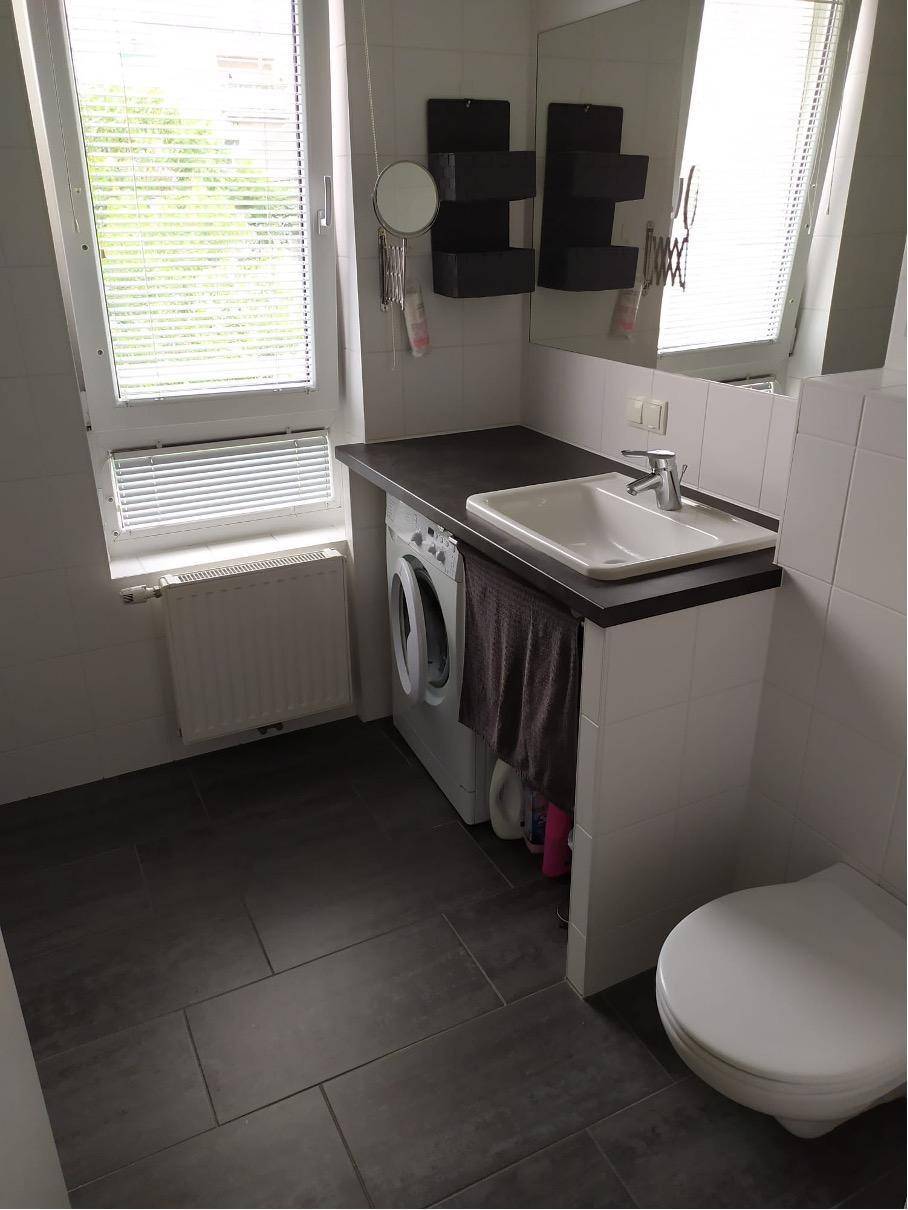 Modernes Badezimmer mit Waschbecken, Toilette und integrierter Waschmaschine unter dem Waschtisch.