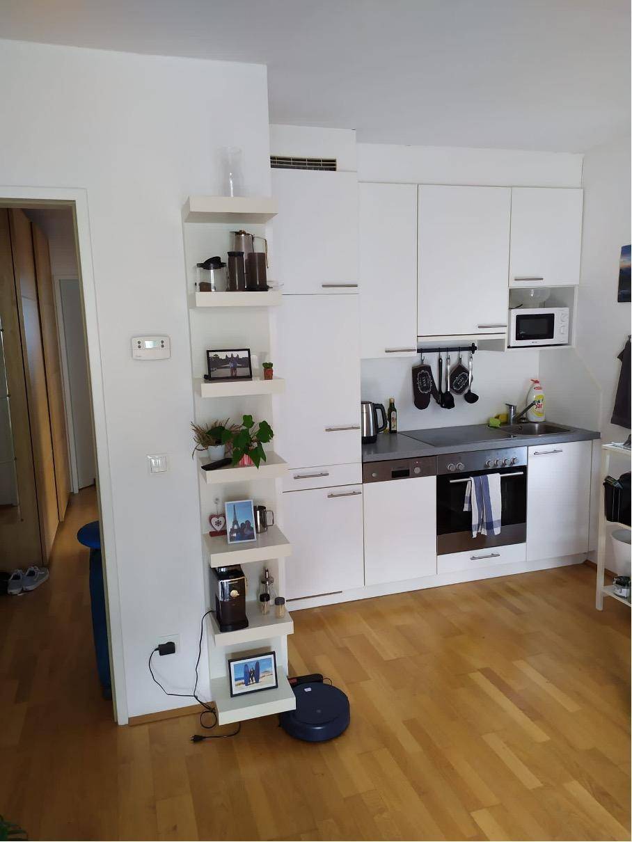 Kompakte, moderne Einbauküche mit weißen Schränken und integrierten Geräten in hellem Ambiente.