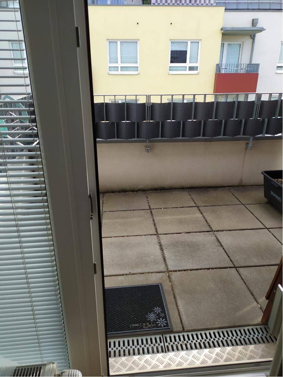 Blick von innen auf eine geflieste Terrasse mit Sichtschutz und angrenzendem Gebäude.