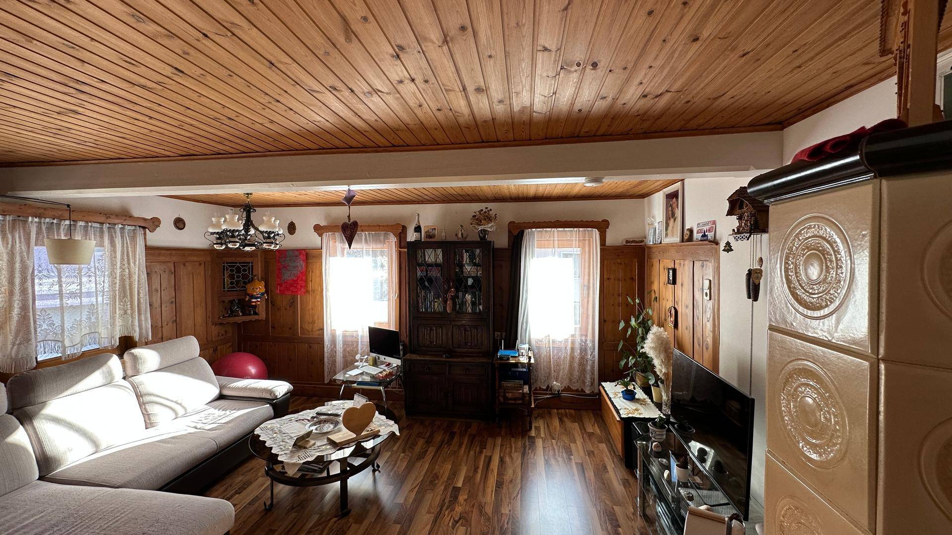 Traditionelles Wohnzimmer mit Kachelofen, Holzdecke und gemütlicher Sitzecke.