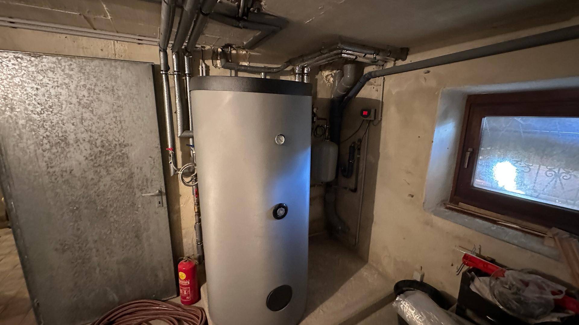 Kellerraum mit Warmwasserspeicher und sichtbaren Rohrleitungen.