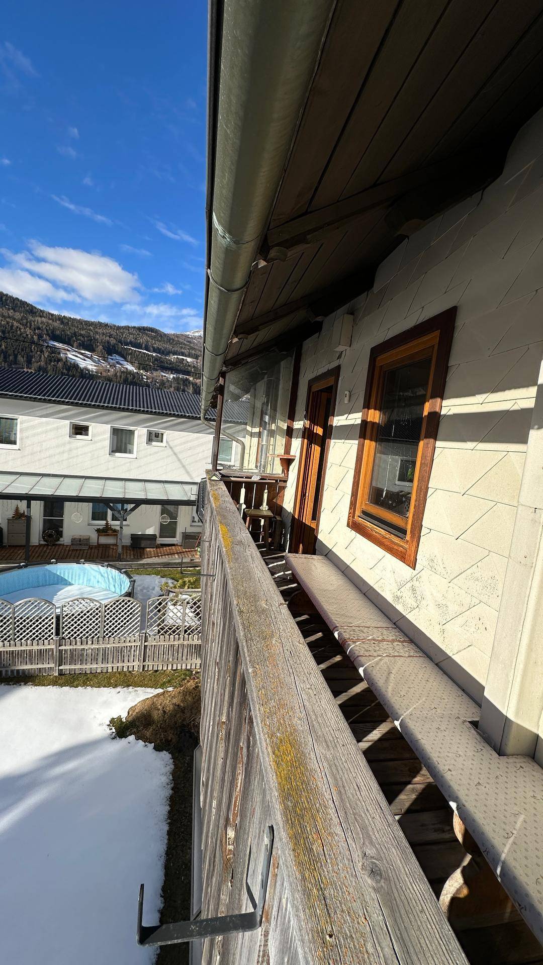 Langer Holzbalkon mit Blick auf die Umgebung und ein nahegelegenes Gebäude.