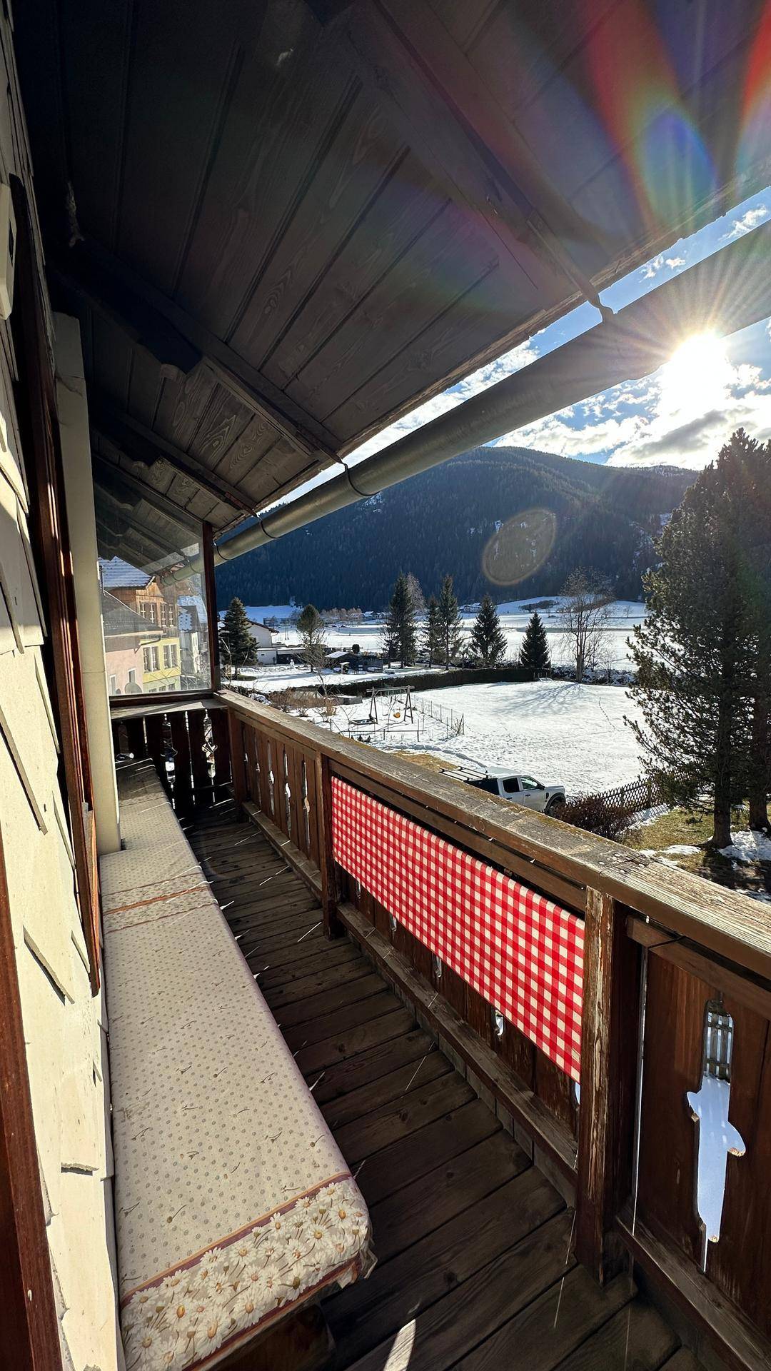 Sonniger Balkon mit Holzboden und weitem Blick auf die verschneite Berglandschaft.