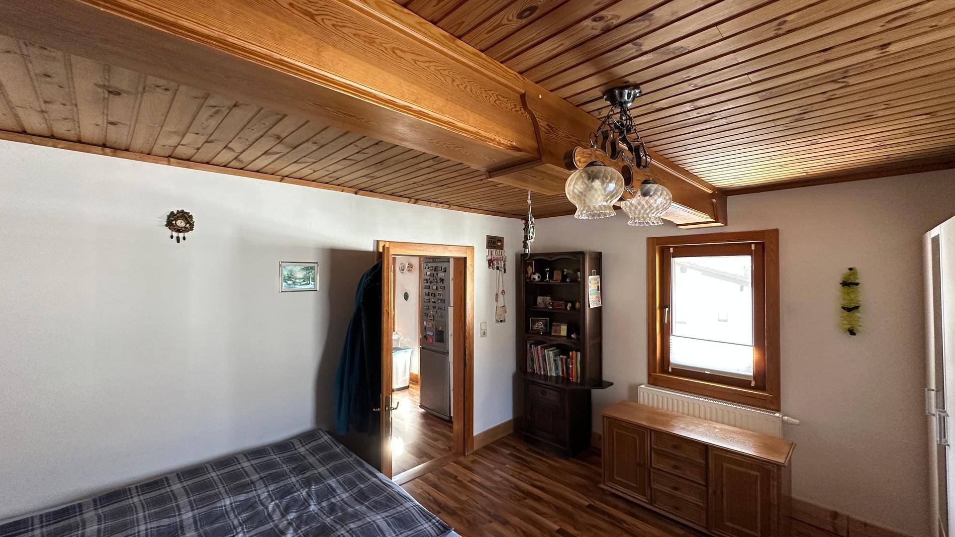 Schlafzimmer mit Holzbalken, Fenster und Blick in den angrenzenden Raum.
