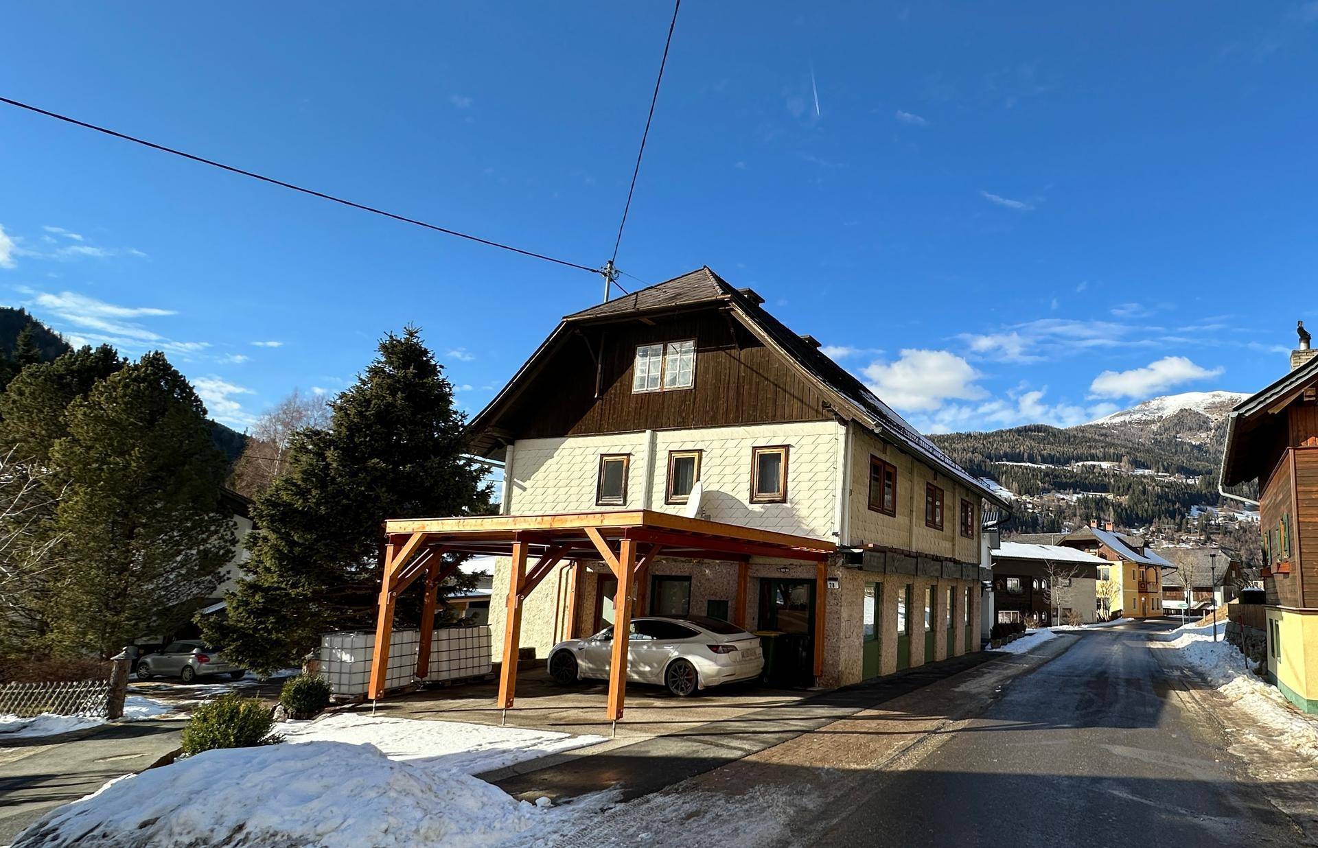 Traditionelles Haus mit Carport und Satteldach in ländlicher Umgebung, umgeben von Schnee und Bergen.
