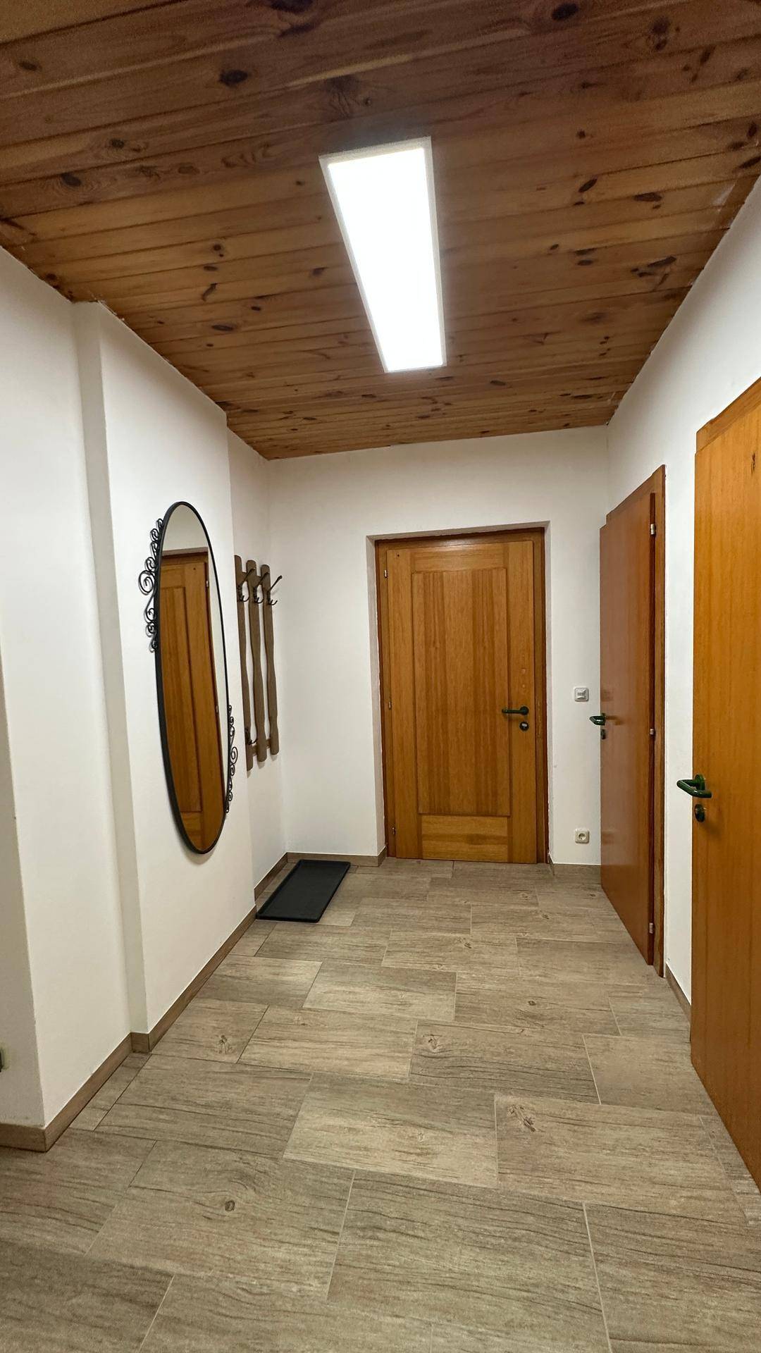 Heller Flur mit Holzdecke, Fliesenboden und einem ovalen Spiegel an der Wand.