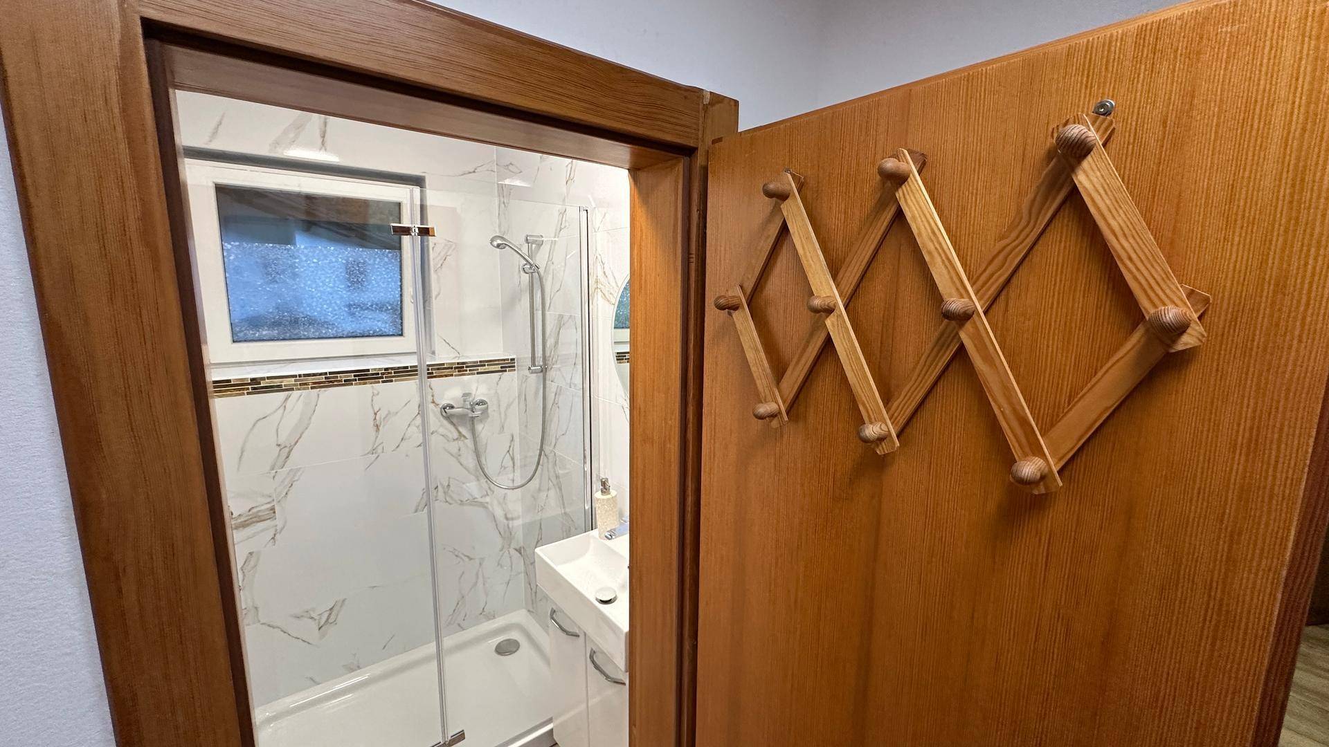 Badezimmer mit Duschkabine, modernen Fliesen und einem Fenster für Tageslicht.