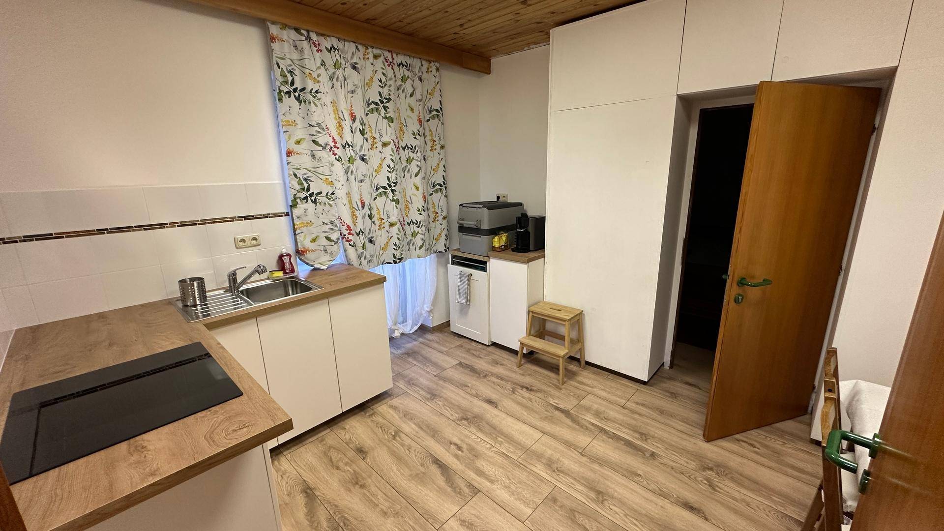 Kleine Küche mit modernen weißen Schränken, Holz-Arbeitsplatte und floralen Vorhängen.