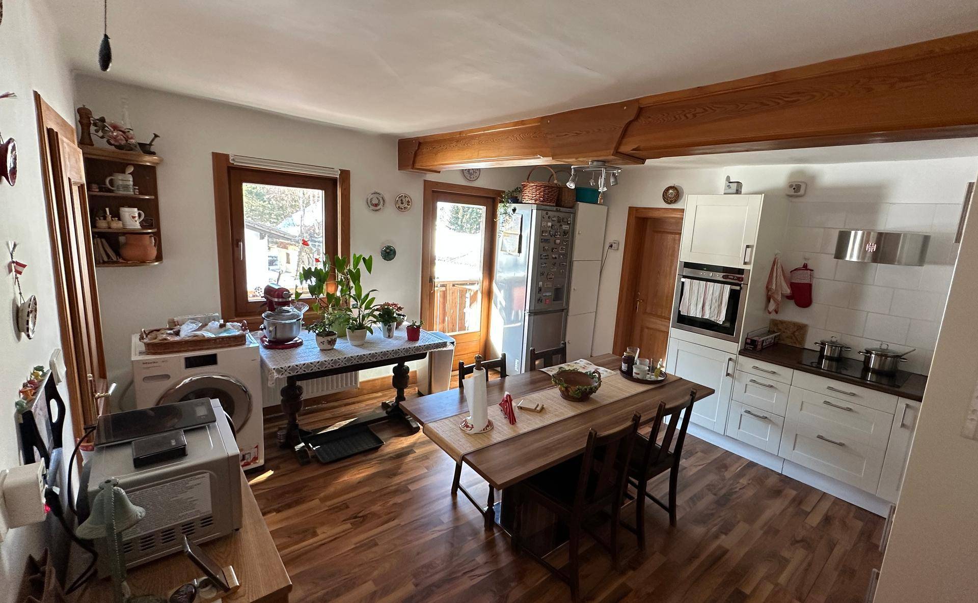 Geräumiger Wohn-Essbereich mit offener Küche, Holzbalken und Zugang zum Balkon.