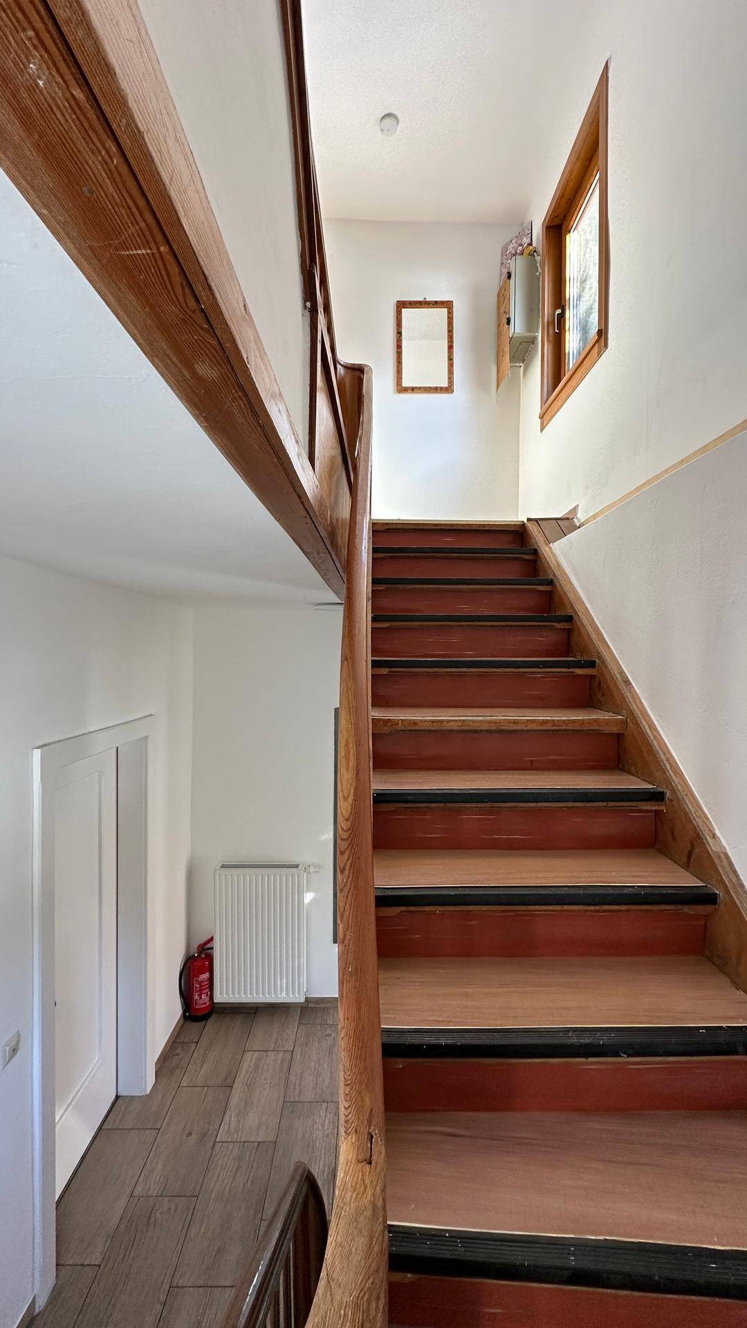 Treppenhaus mit Holztreppe und Fenster, das Tageslicht hereinlässt.