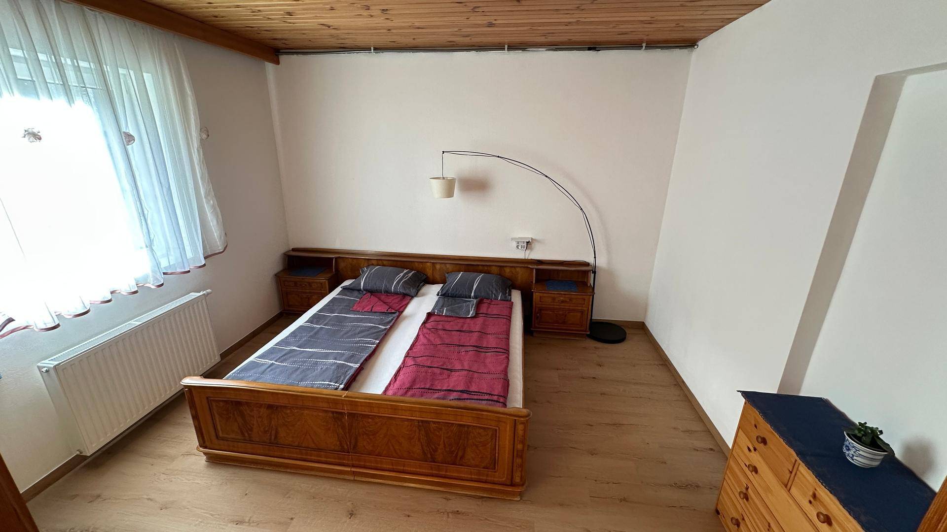 Schlafzimmer mit Doppelbett, Holzdecke und Laminatboden, hell durch großes Fenster.