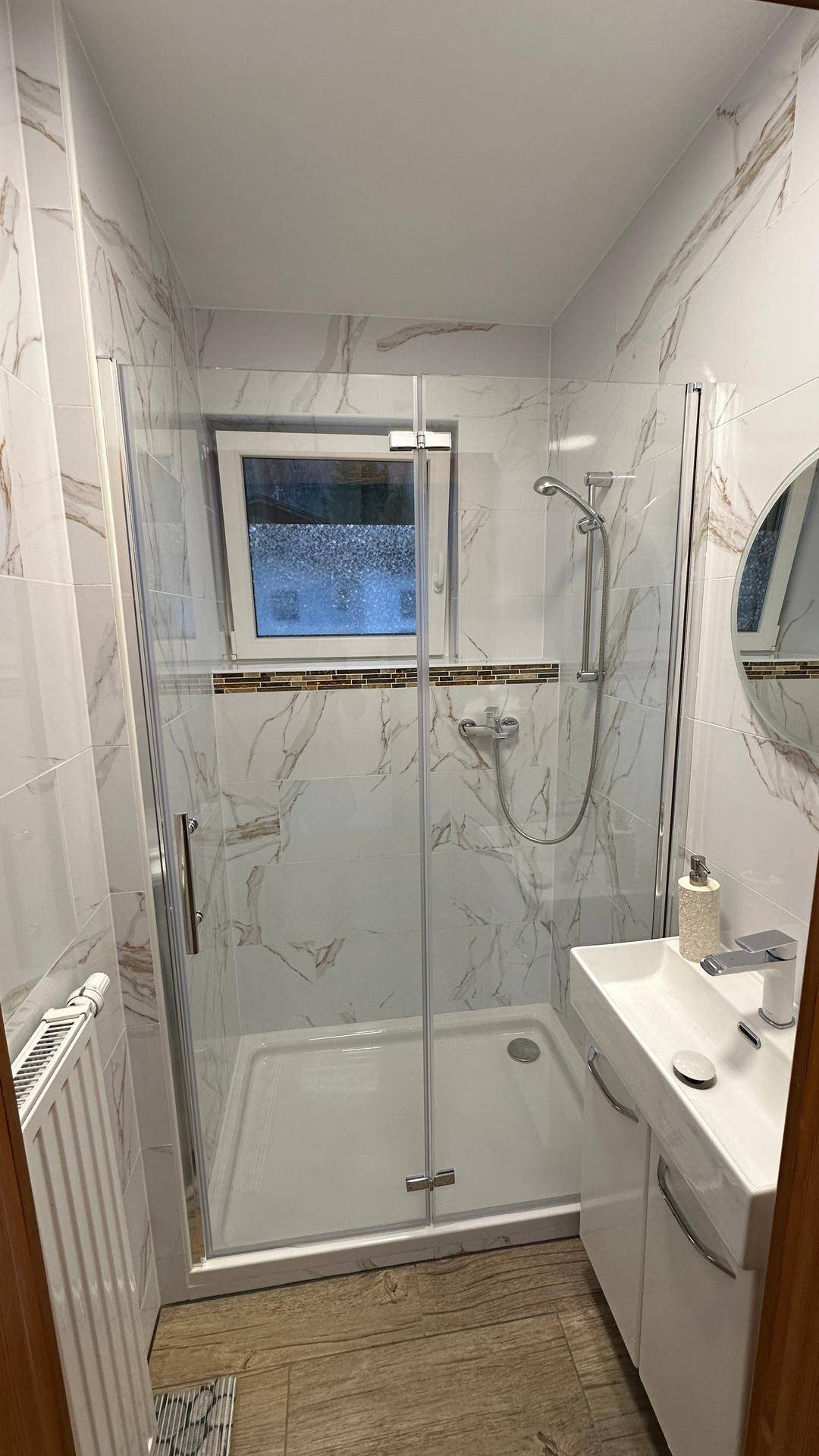 Duschbad mit Glasduschkabine, modernen Marmorfliesen und Fenster.