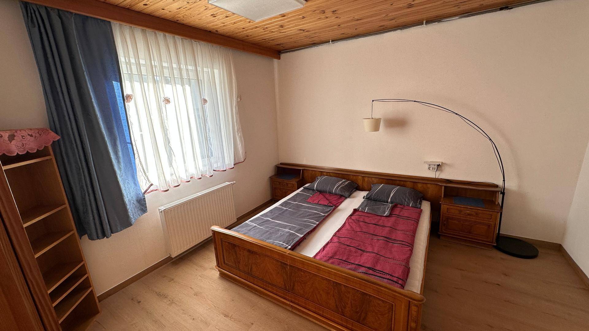 Helles Schlafzimmer mit Holzdecke, Laminatboden und großem Fenster mit Vorhängen.