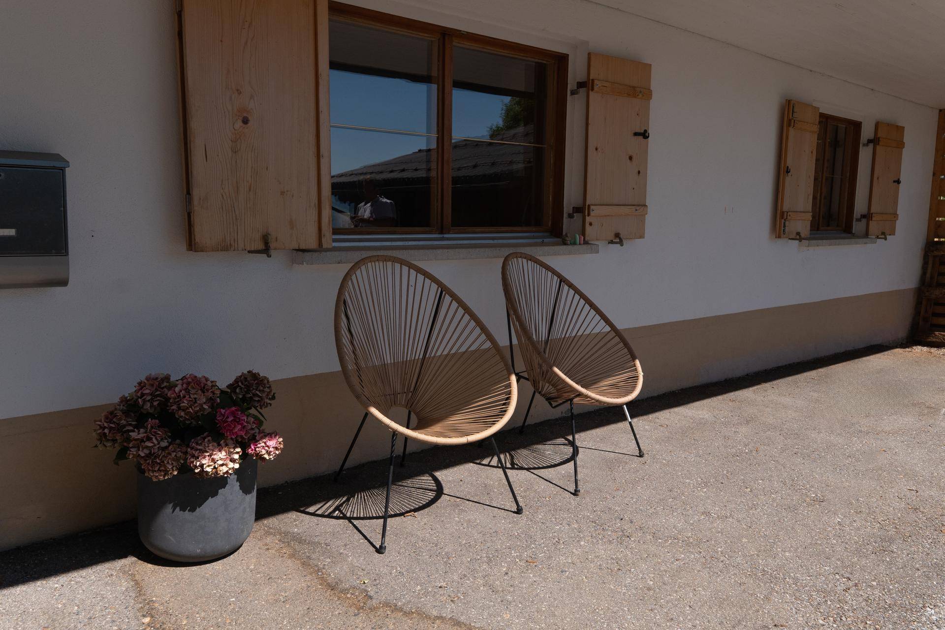 Moderner Sitzbereich auf der gepflasterten Terrasse mit zwei Designerstühlen und Blumenkübel.