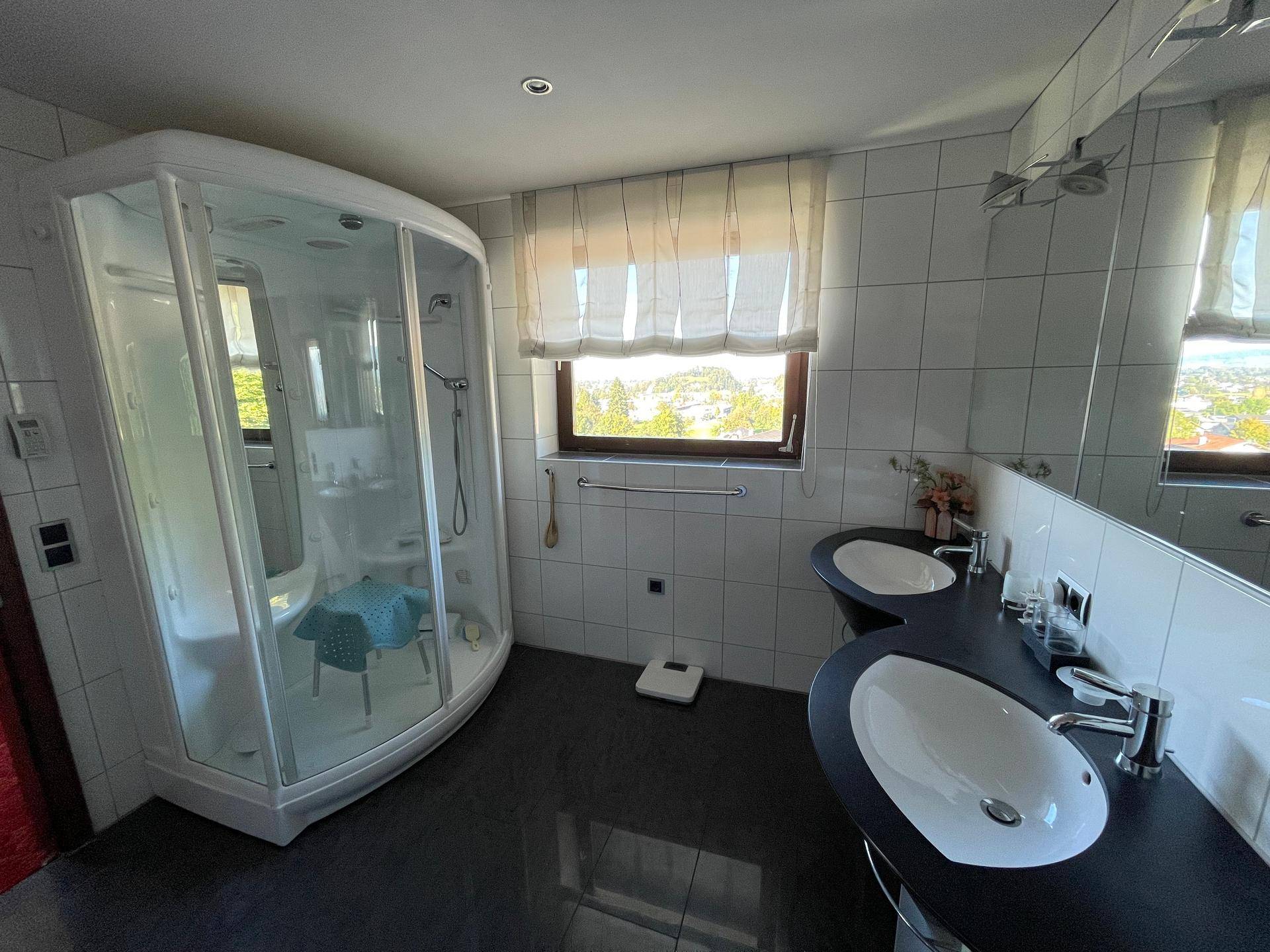 Badezimmer mit Eckduschkabine, Doppelwaschbecken und einem Fenster mit Ausblick.