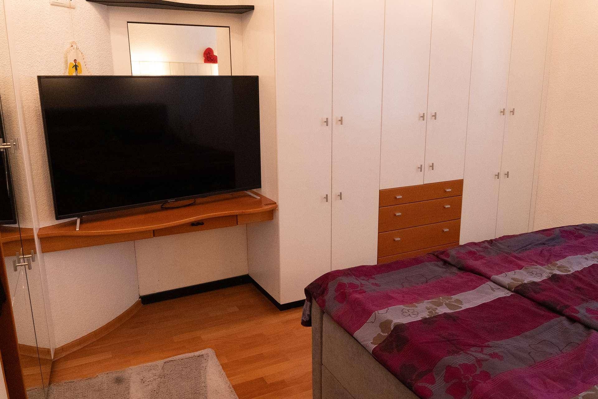 Gemütliches Schlafzimmer mit Einbauschränken, Holzboden und Fernseher.