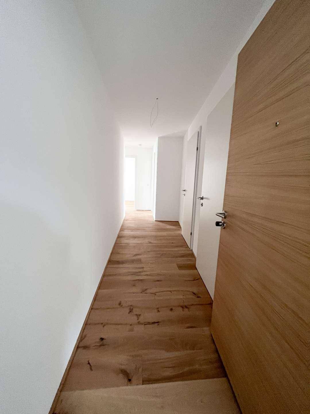 Heller Flur mit Holzdielenboden und weißen Wänden, der zu weiteren Räumen führt.
