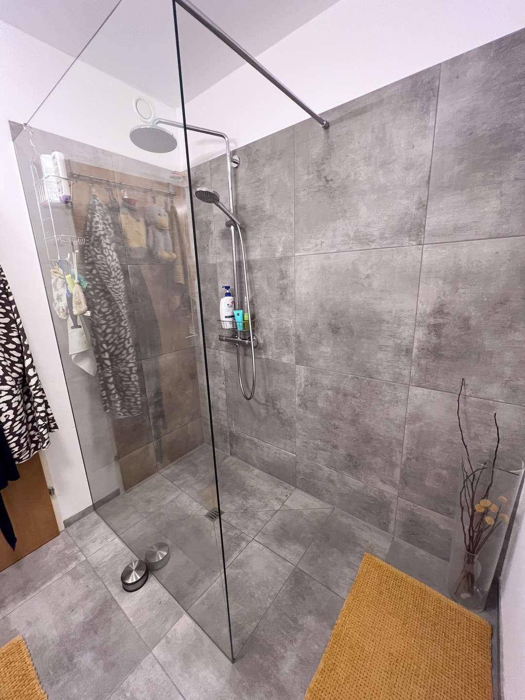 Moderne begehbare Dusche mit großen grauen Fliesen und Glasabtrennung.