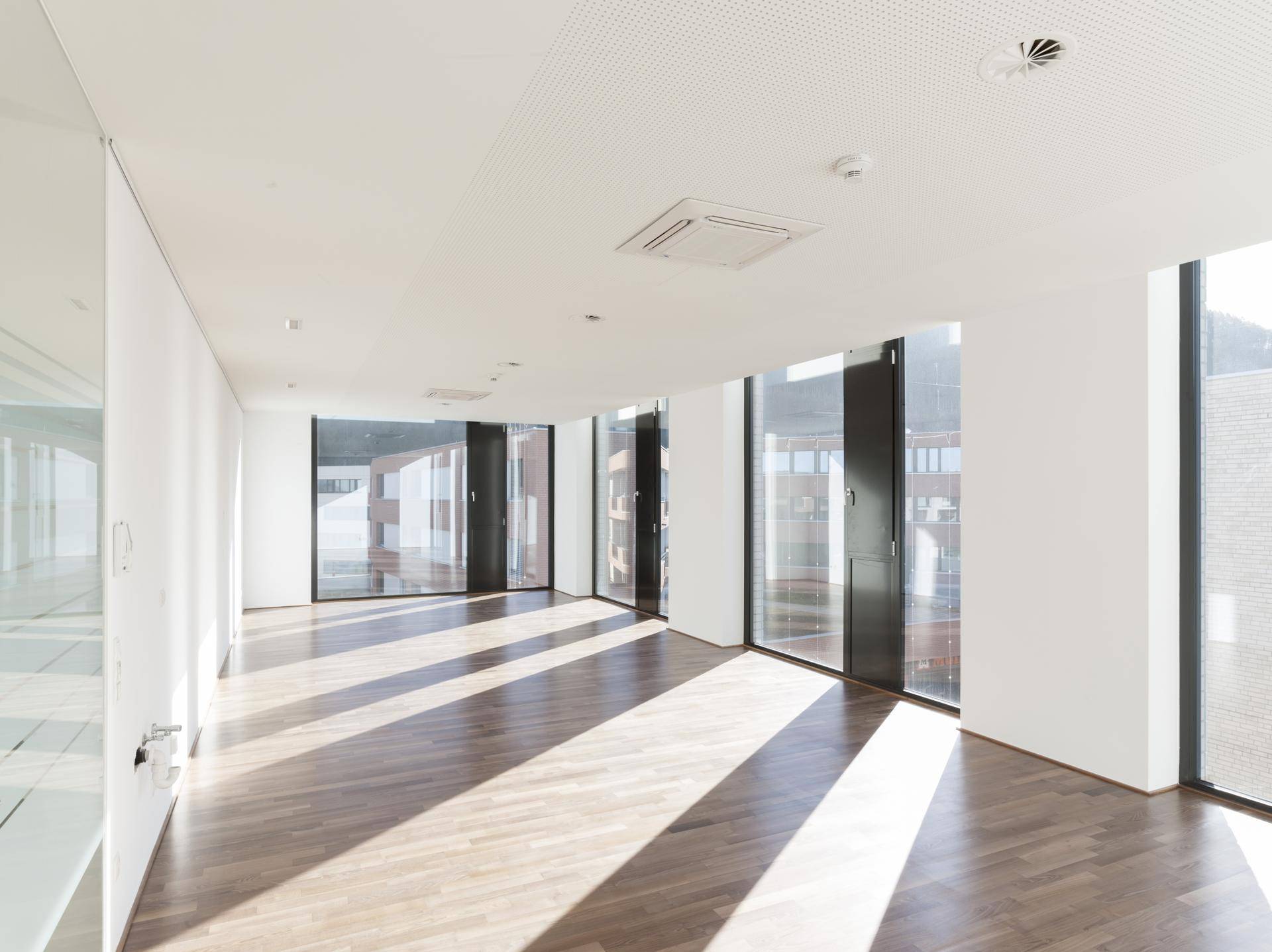 Geräumiger, heller Bürobereich mit Holzboden und großen Fenstern, die viel Sonnenlicht hereinlassen und eine offene Atmosphäre schaffen.