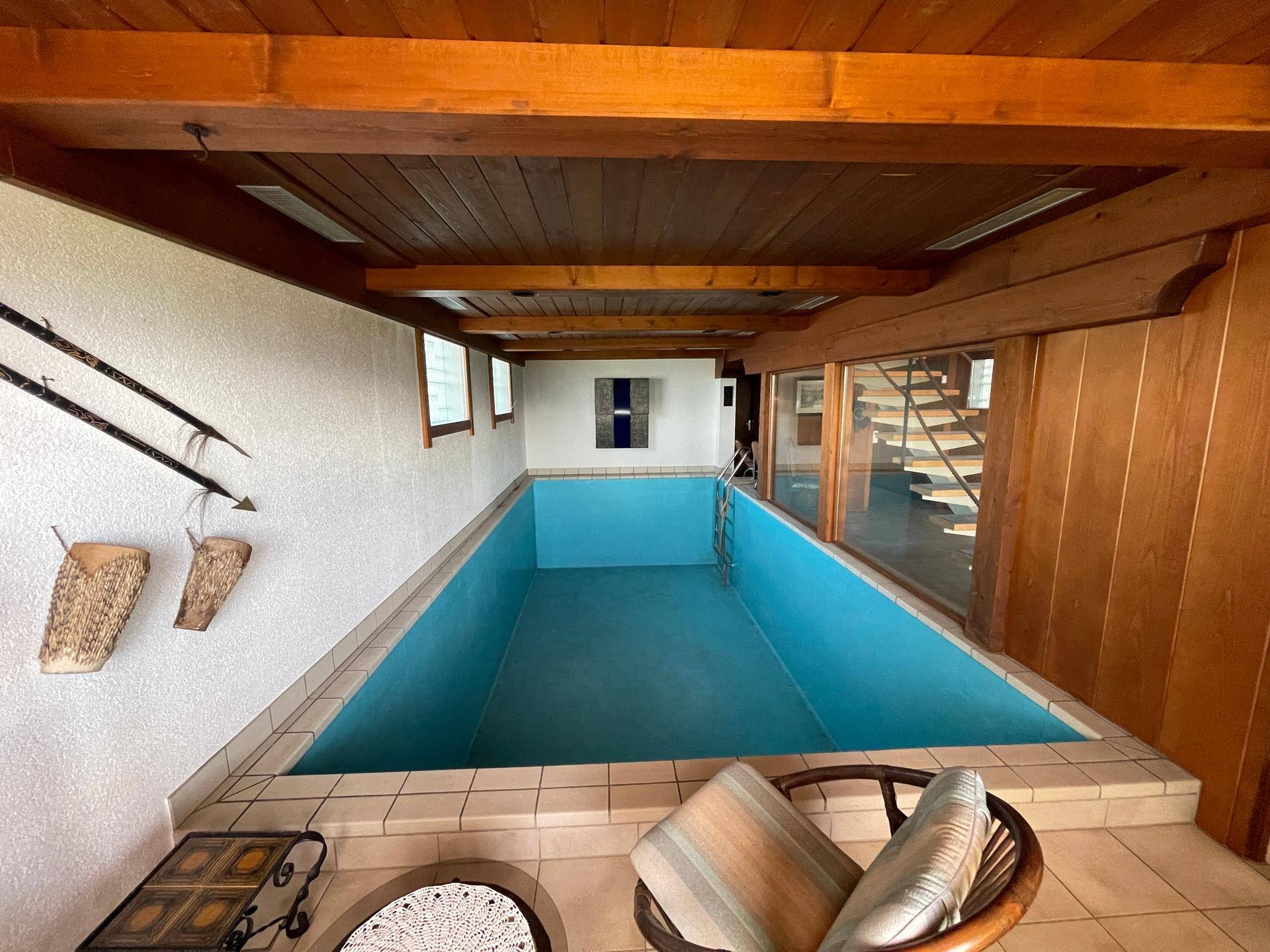 Innenpool mit blauen Fliesen, Holzdecke und Blick auf eine Wendeltreppe.