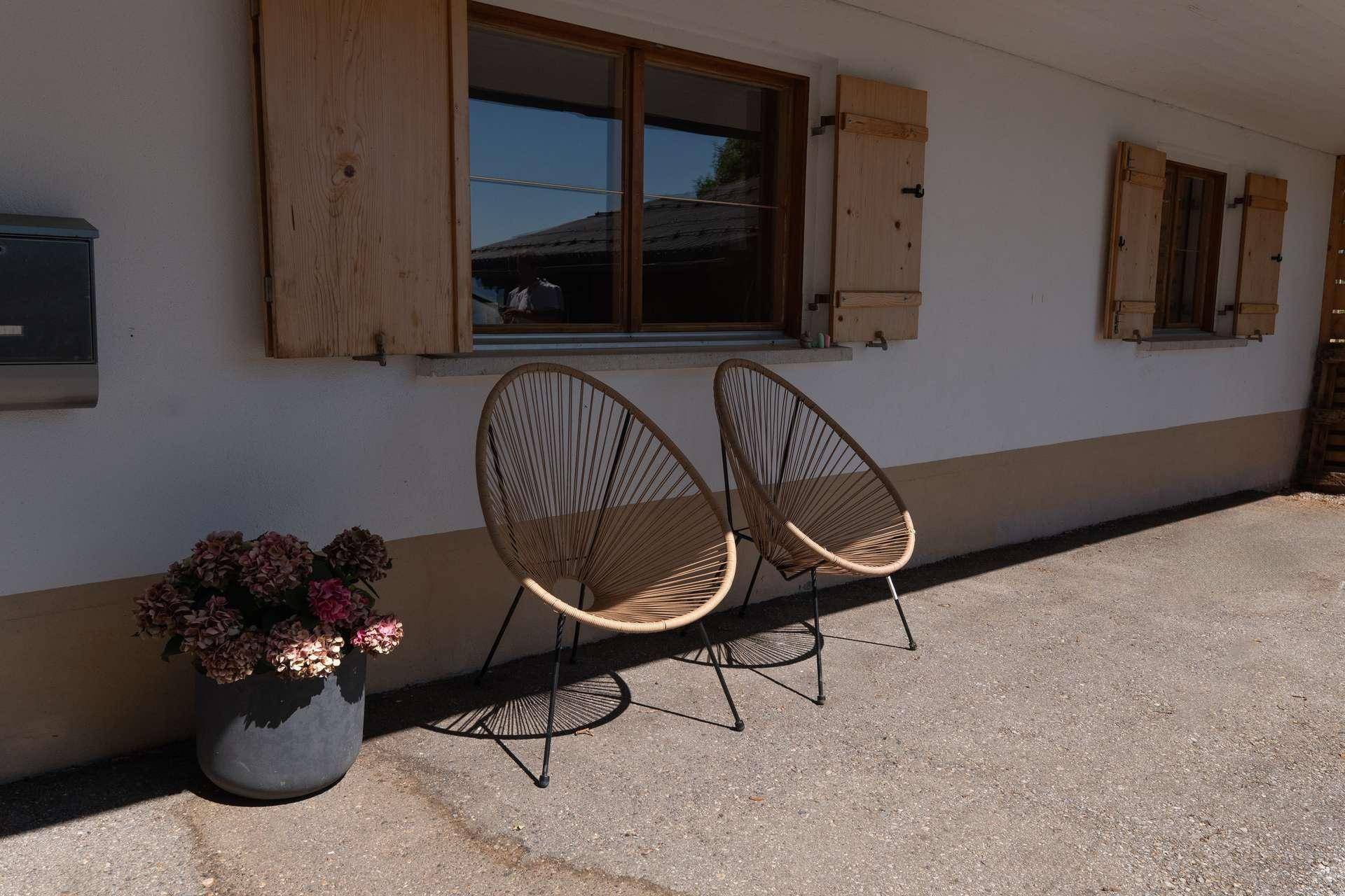 Moderner Sitzbereich im Freien mit zwei Stühlen und Blumenkübel vor der Hausfassade.