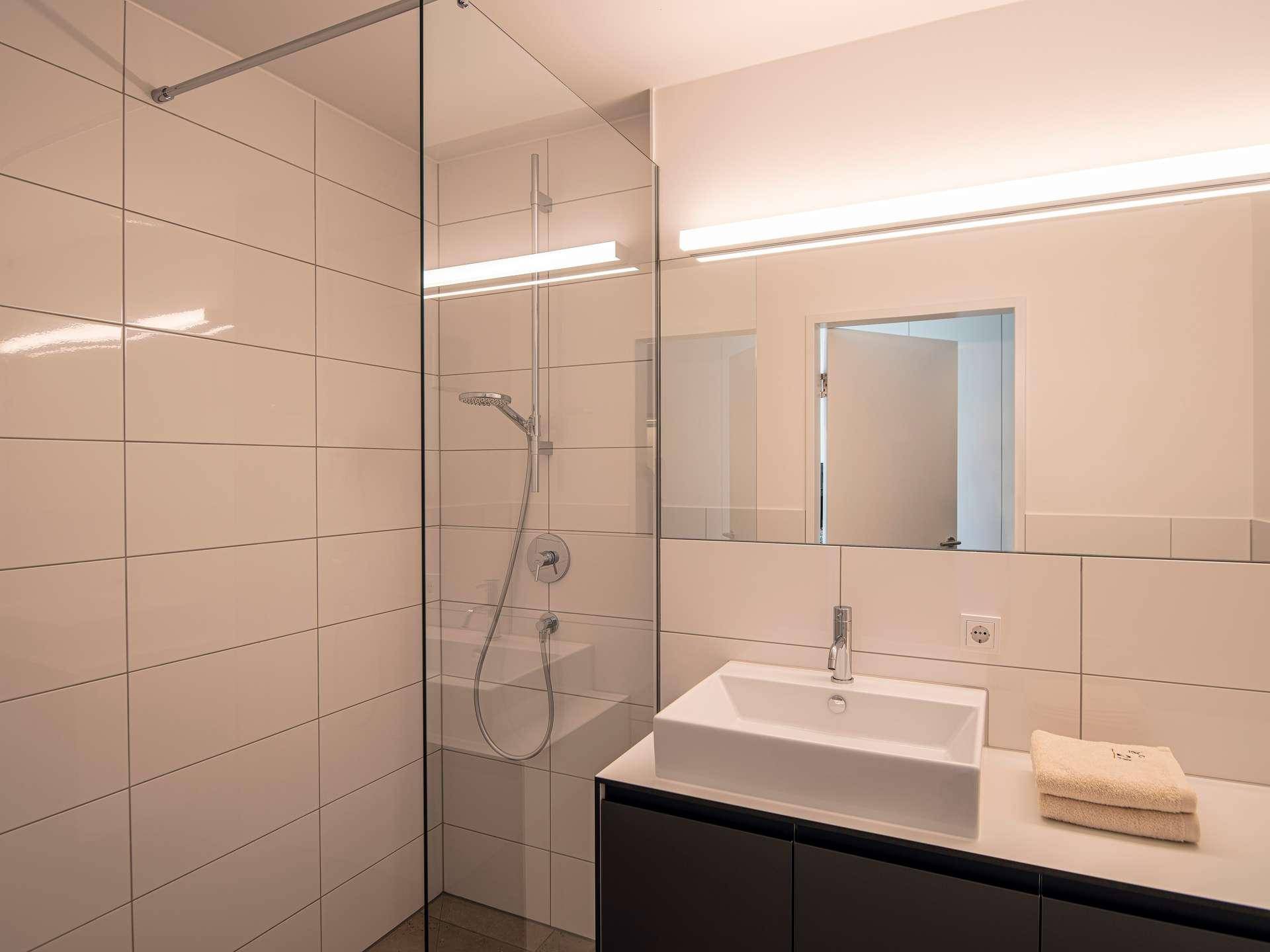 Modernes Badezimmer mit begehbarer Dusche, großem Spiegel und eleganten Fliesen.