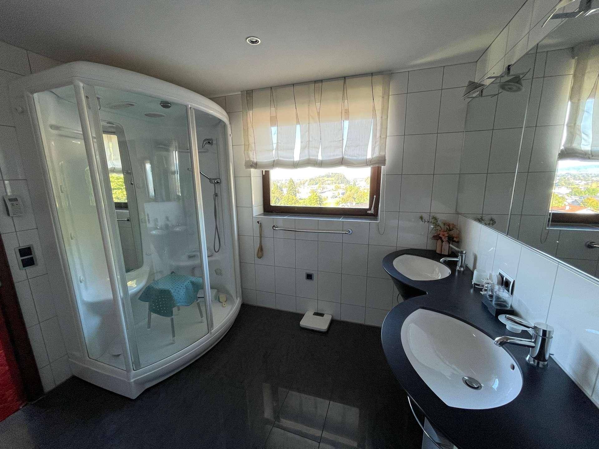 Modernes Badezimmer mit Duschkabine, Doppelwaschbecken und Fenster mit Ausblick.