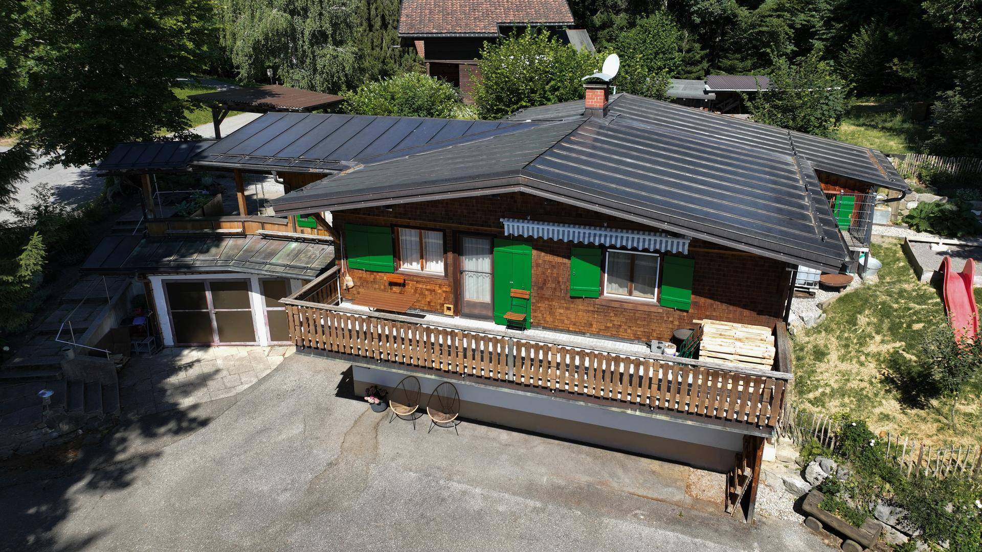 Luftaufnahme des Holzchalets mit Solaranlage auf dem Dach und umliegender grüner Landschaft.