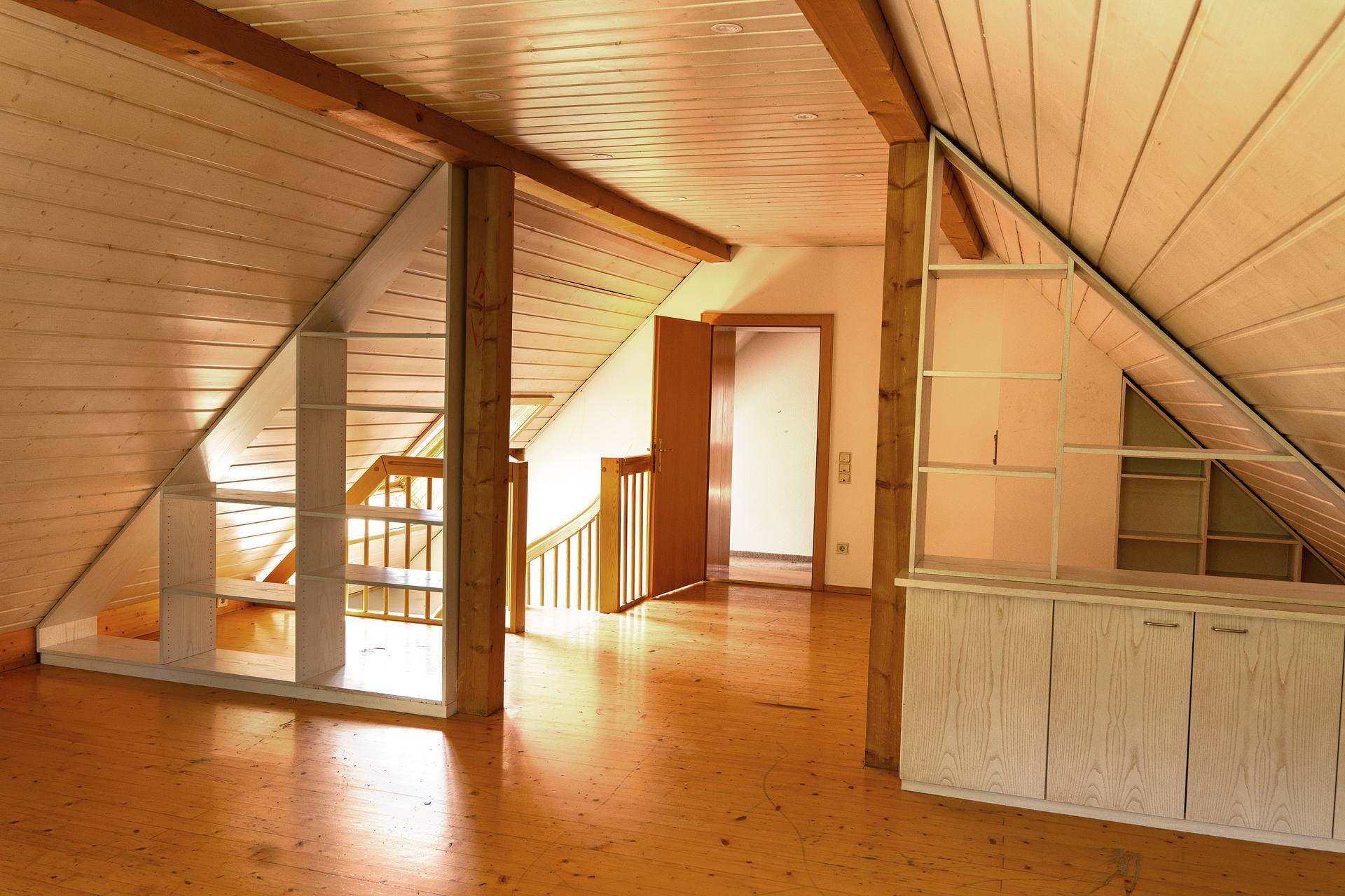 Dachbodenraum mit Holzboden und schrägen Wänden, der den Zugang zu einer Holztreppe zeigt.
