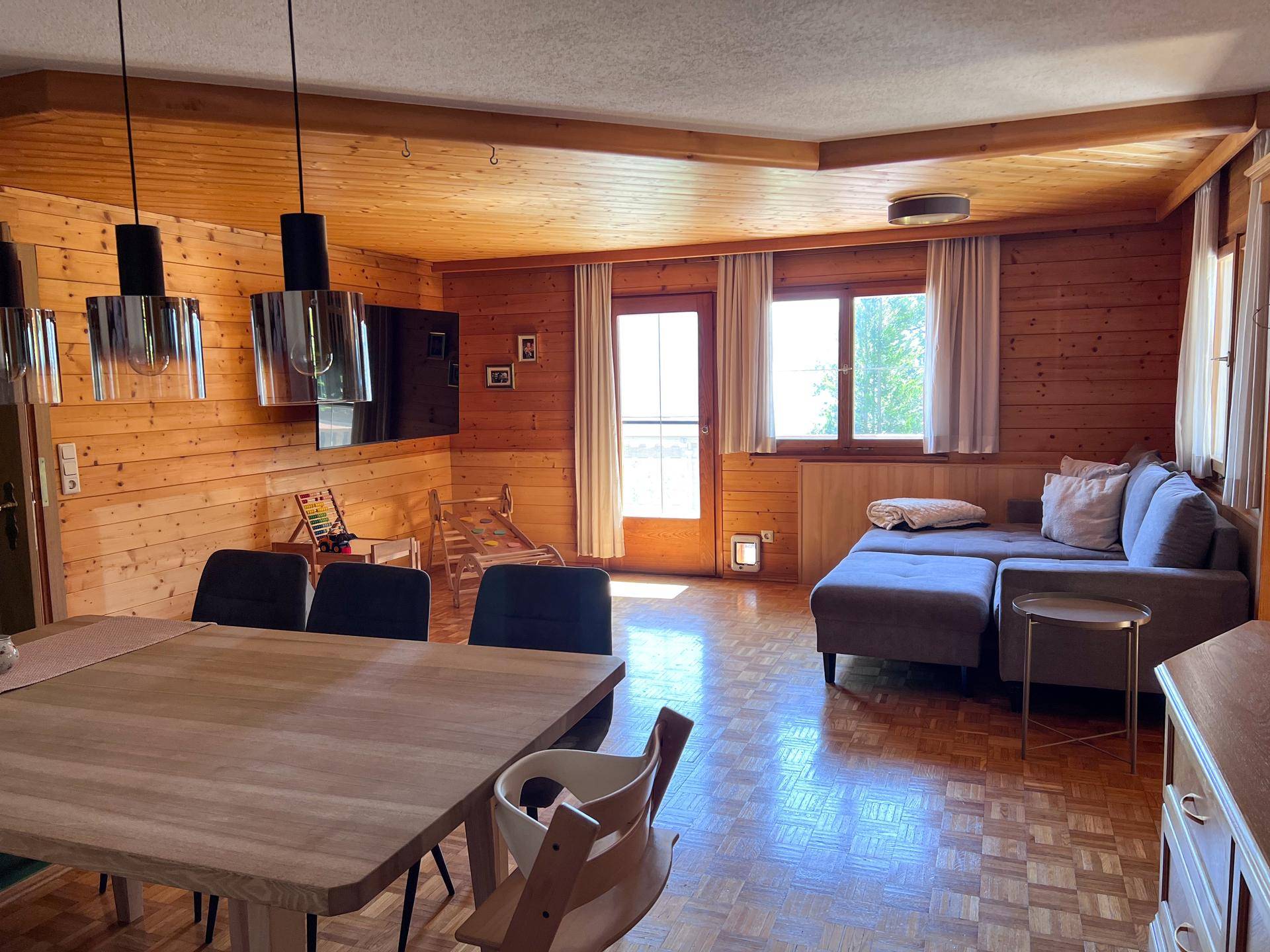 Geräumiger Wohn-Essbereich mit Holzvertäfelung, großem Esstisch und gemütlichem Sofa.