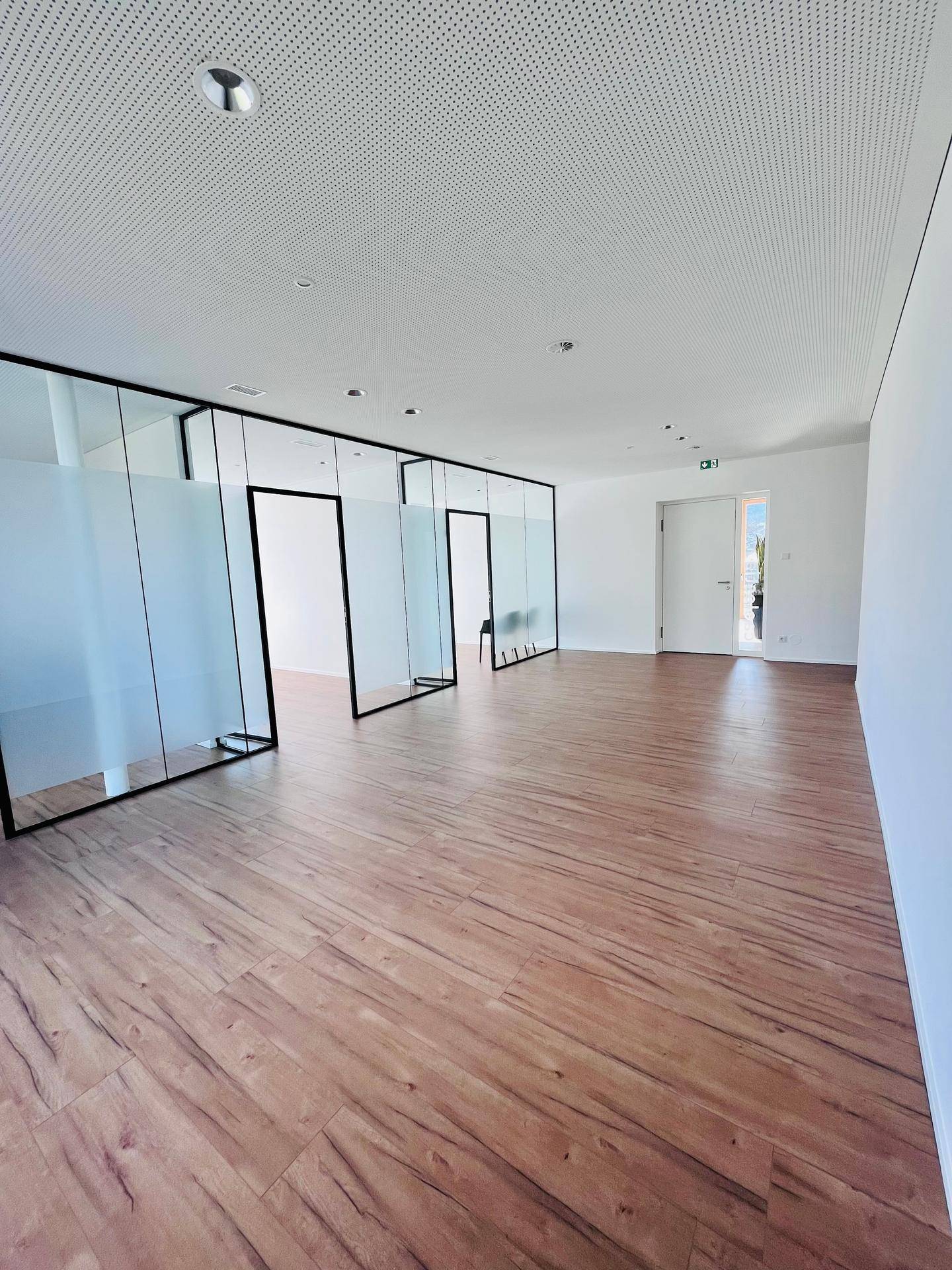 Heller, offener Büroraum mit modernen Glasabtrennungen und Holzboden, bereit zur individuellen Gestaltung.