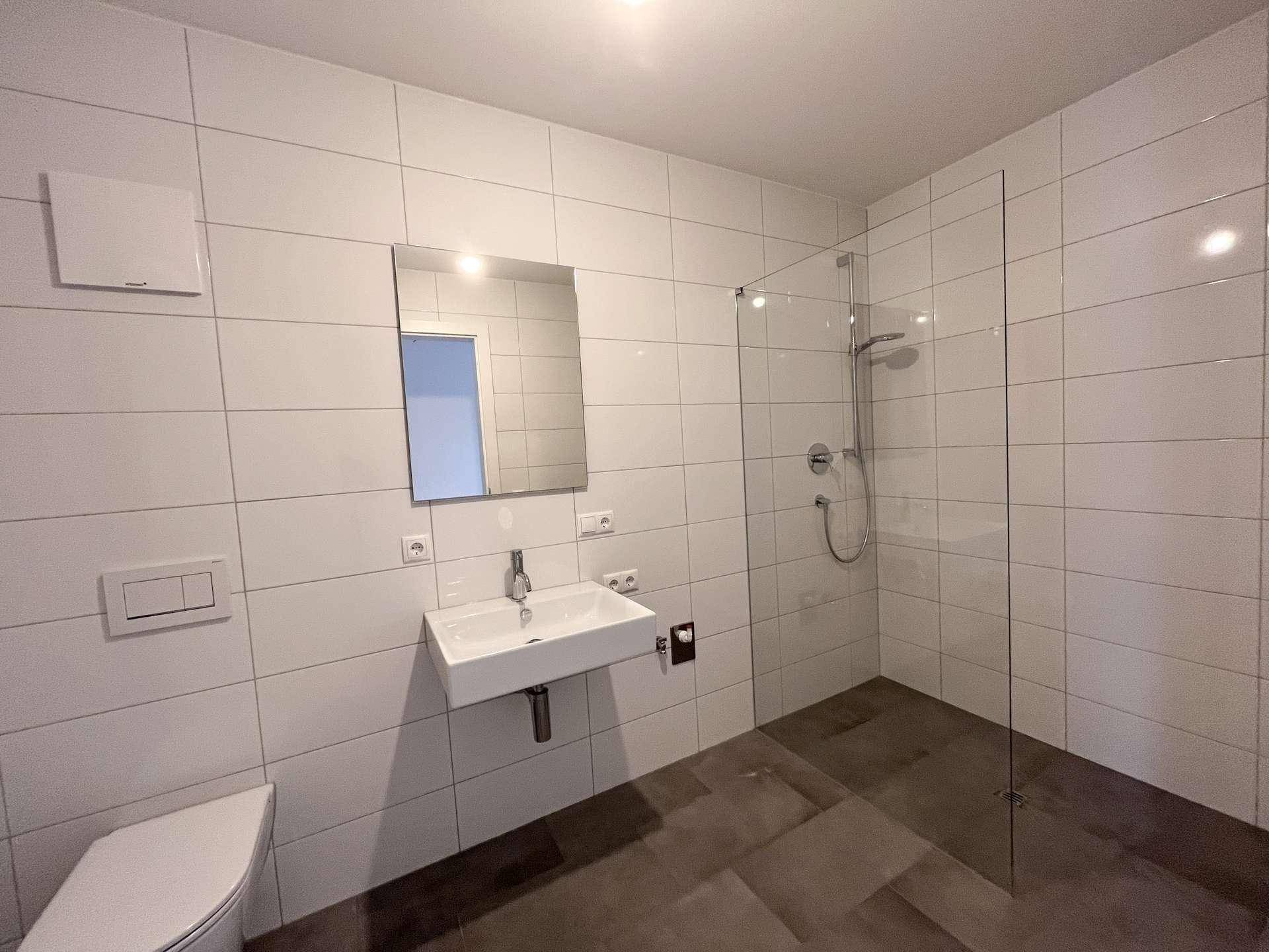 Modernes Badezimmer mit weißen Fliesen, ebenerdiger Dusche und wandhängendem WC.