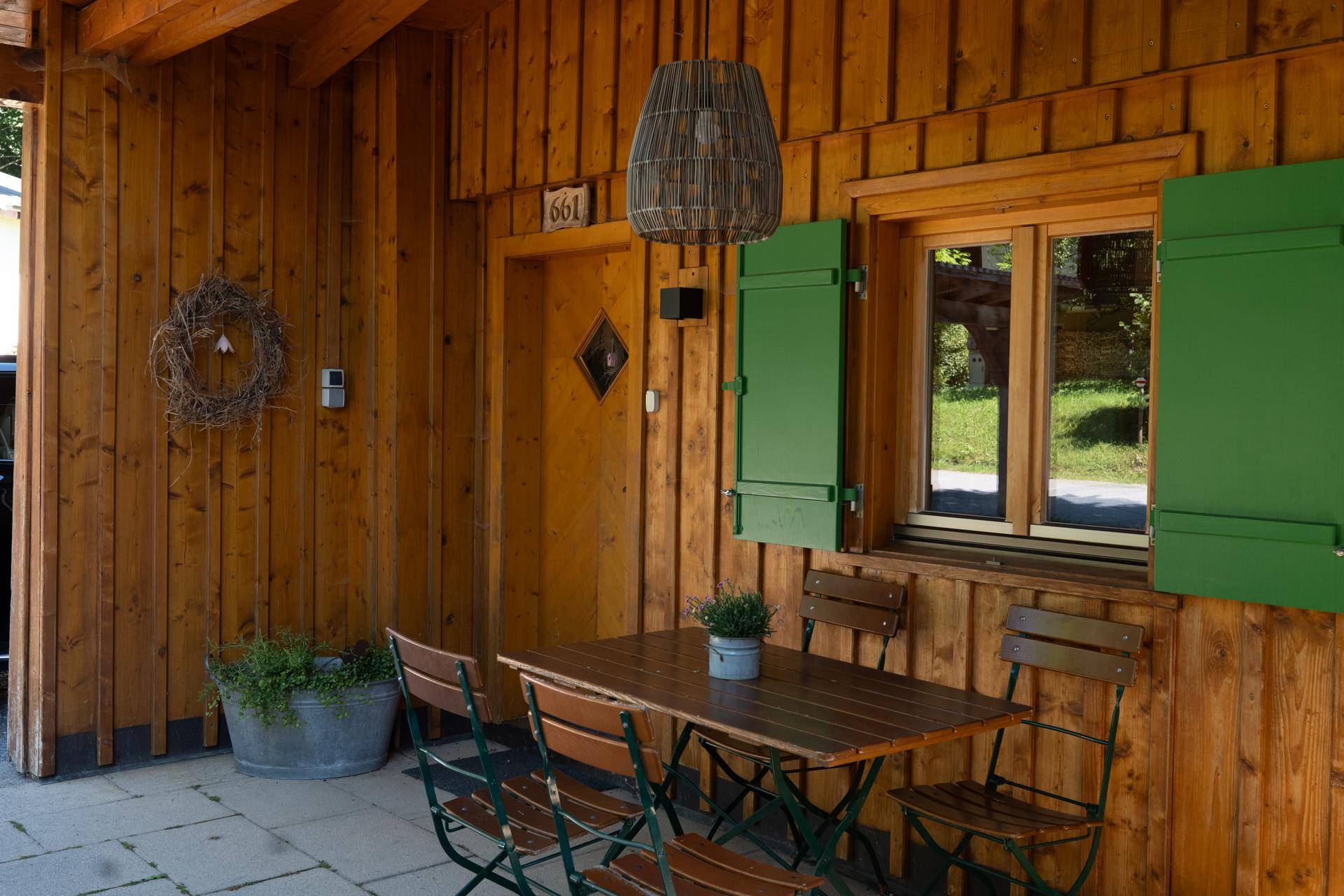 Gepflasterte Terrasse mit Holztisch und Stühlen vor dem Hauseingang mit Holzverkleidung.