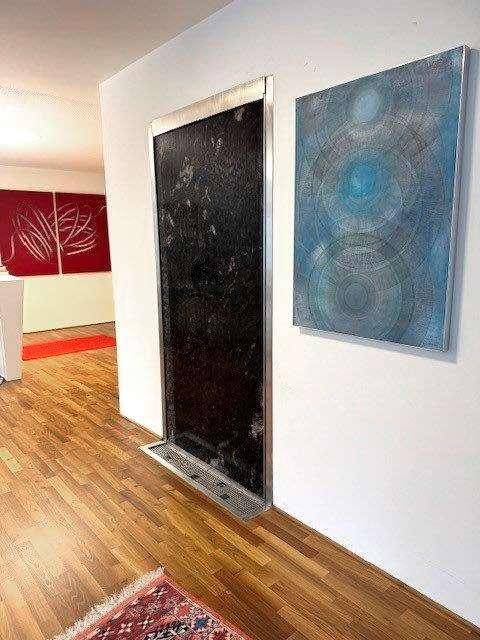 Flur mit Holzboden, Kunstwerken und einem dekorativen Wasserelement an der Wand, inklusive Aufzug.