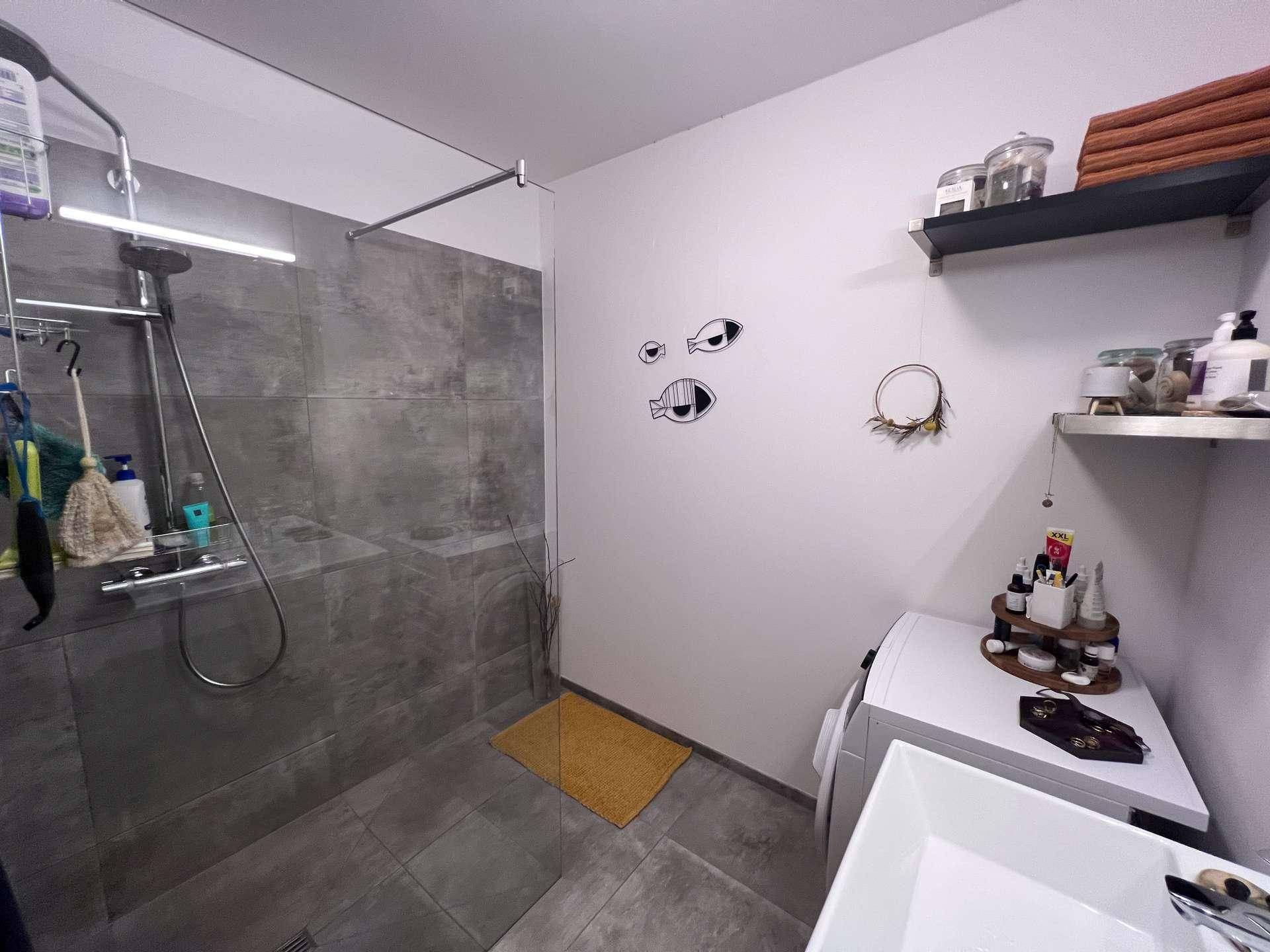 Funktionales Badezimmer mit begehbarer Dusche, Waschbecken und integrierter Waschmaschine.