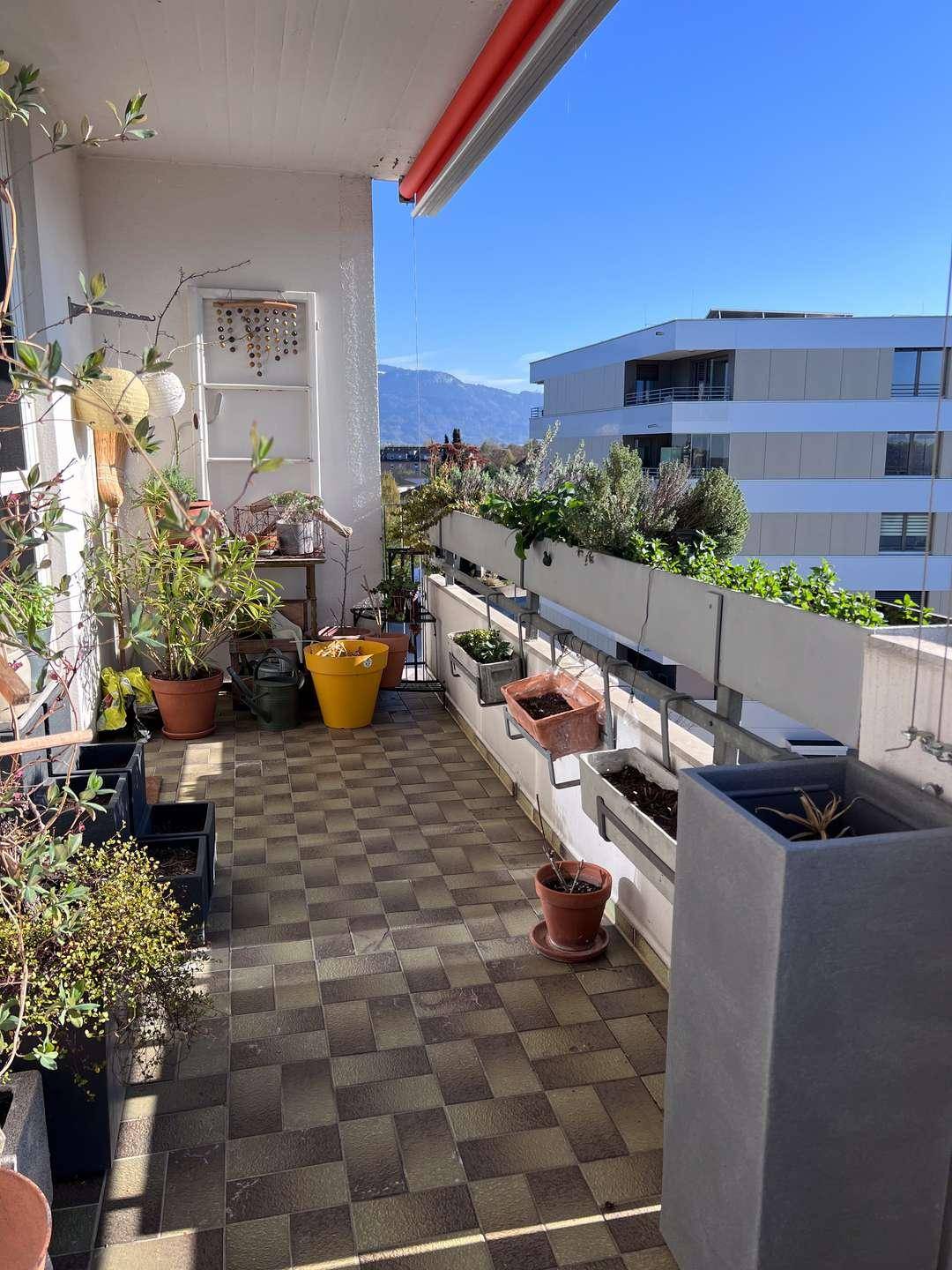 Bepflanzter Balkon mit Fliesenboden und Blick auf die umliegende Landschaft und Berge.