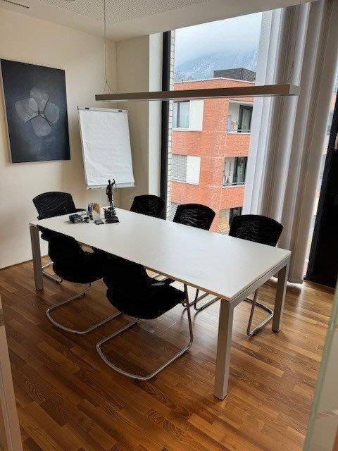 Konferenzraum mit großem Tisch, modernen Stühlen und Blick auf die Umgebung durch das Fenster, ideal für Besprechungen.