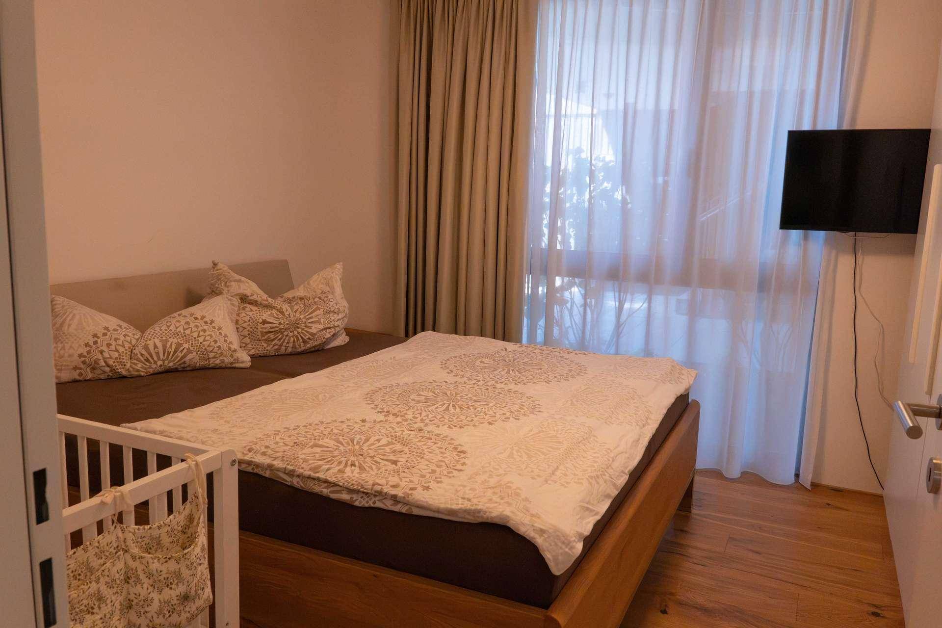Helles Schlafzimmer mit Doppelbett, Babybett und Holzboden.