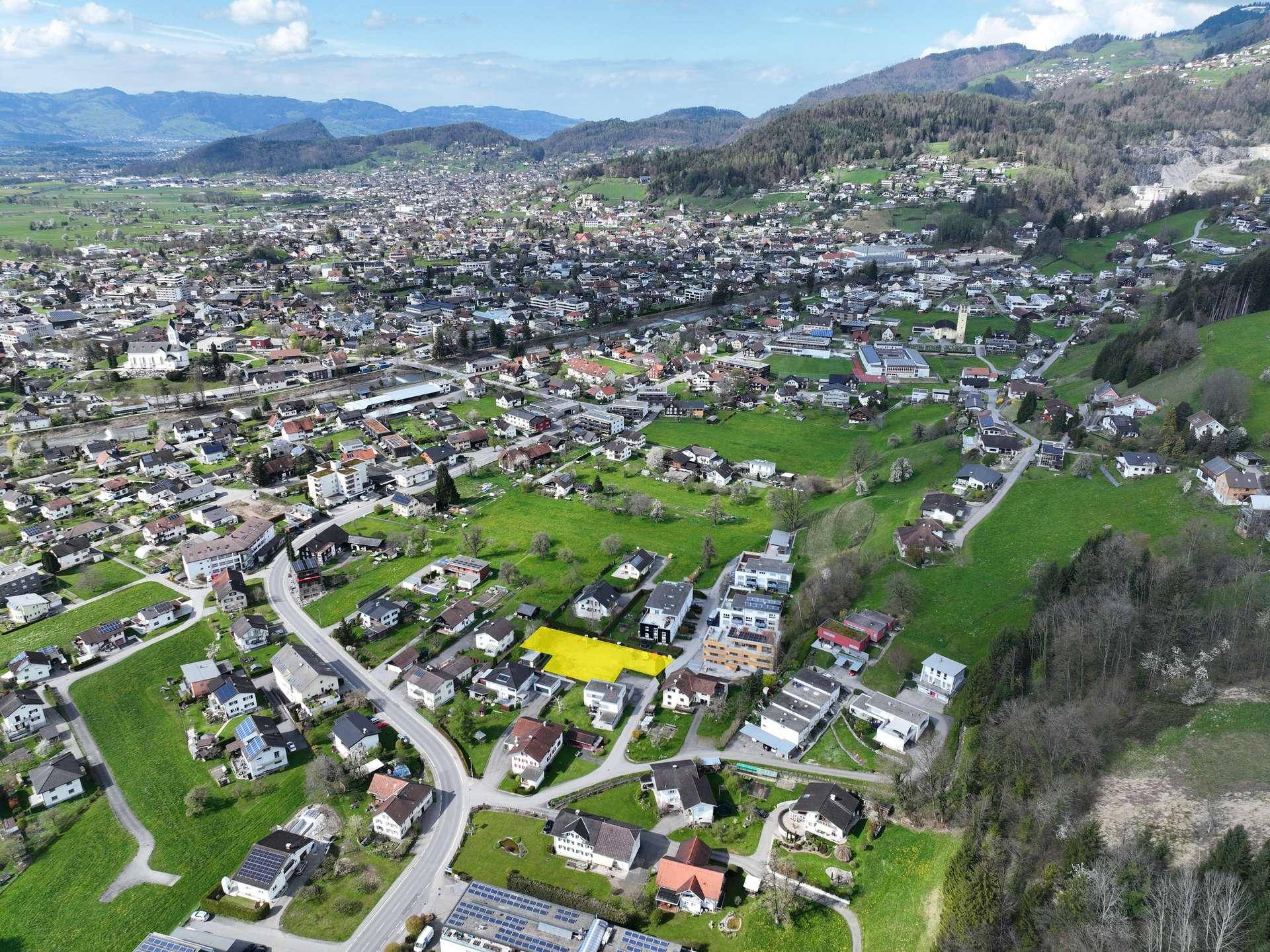 Weitläufige Luftaufnahme einer Gemeinde mit Wohngebieten, grünen Landschaften und Bergblick.