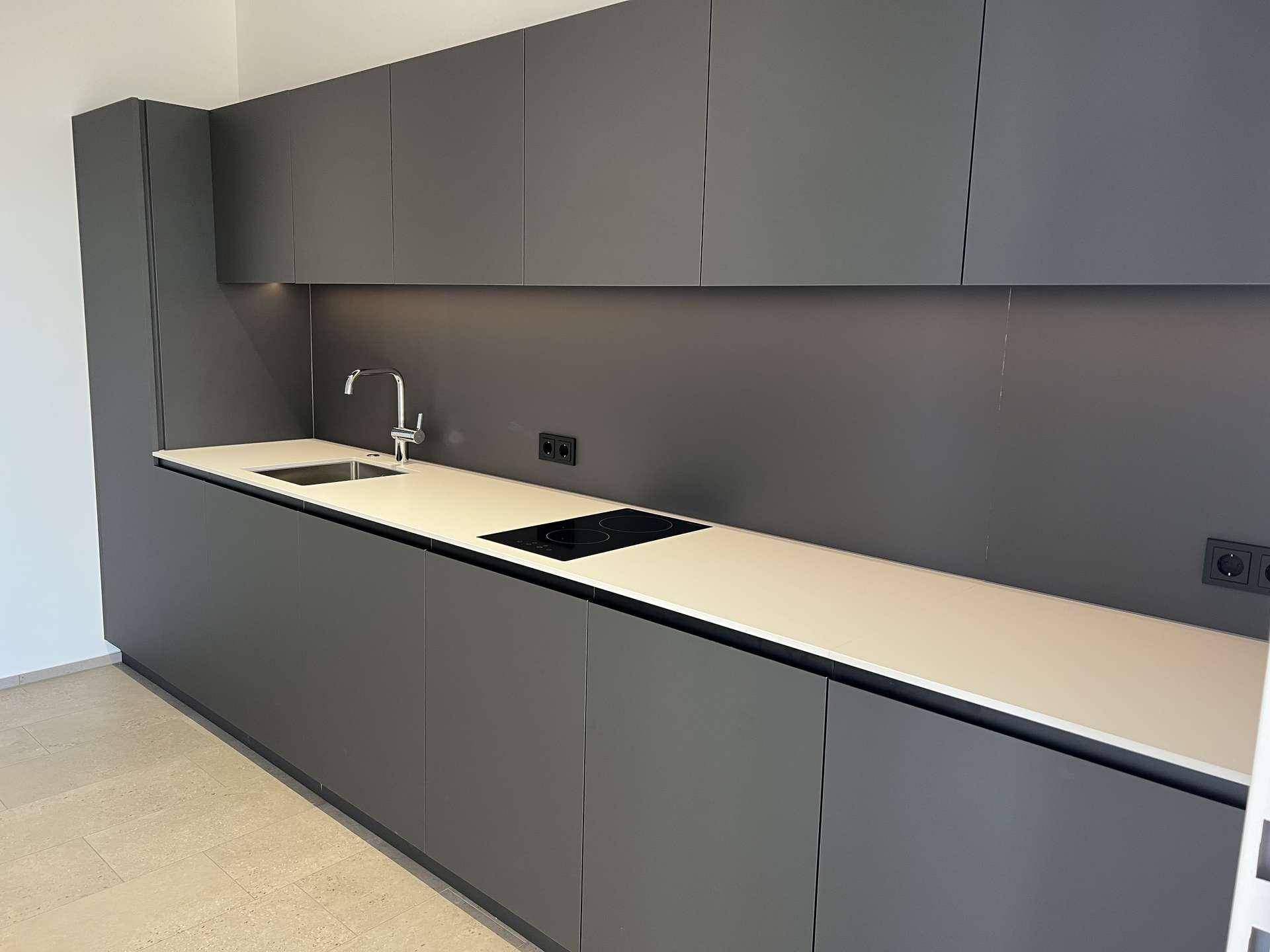 Moderne Küche mit grauen, grifflosen Schränken, heller Arbeitsplatte und integriertem Kochfeld.