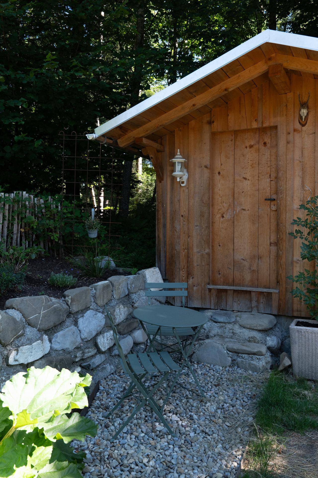 Gemütliche Sitzecke im Garten neben einem Holzschuppen mit Hirschgeweih-Dekoration.