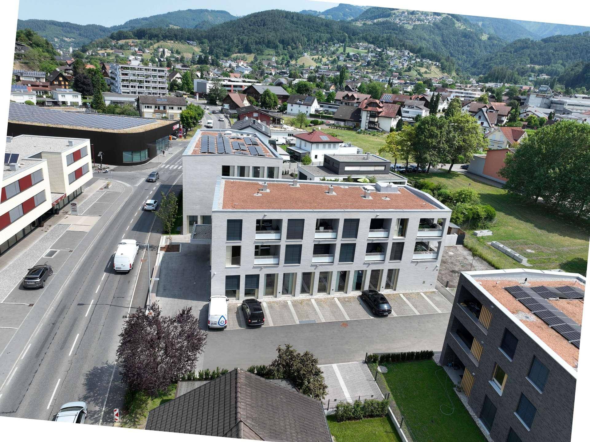 Vogelperspektive auf ein modernes Gebäude mit Flachdach und Solarpaneelen, umgeben von Natur und Straße.