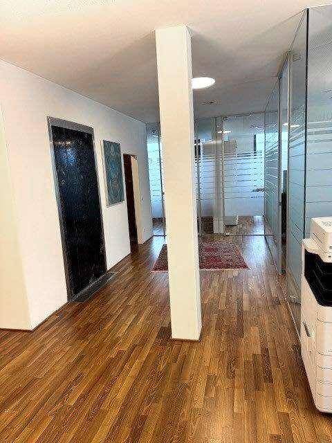 Langer Flur mit Holzboden, Glaswänden und Aufzug, der zu weiteren Büroräumen führt.
