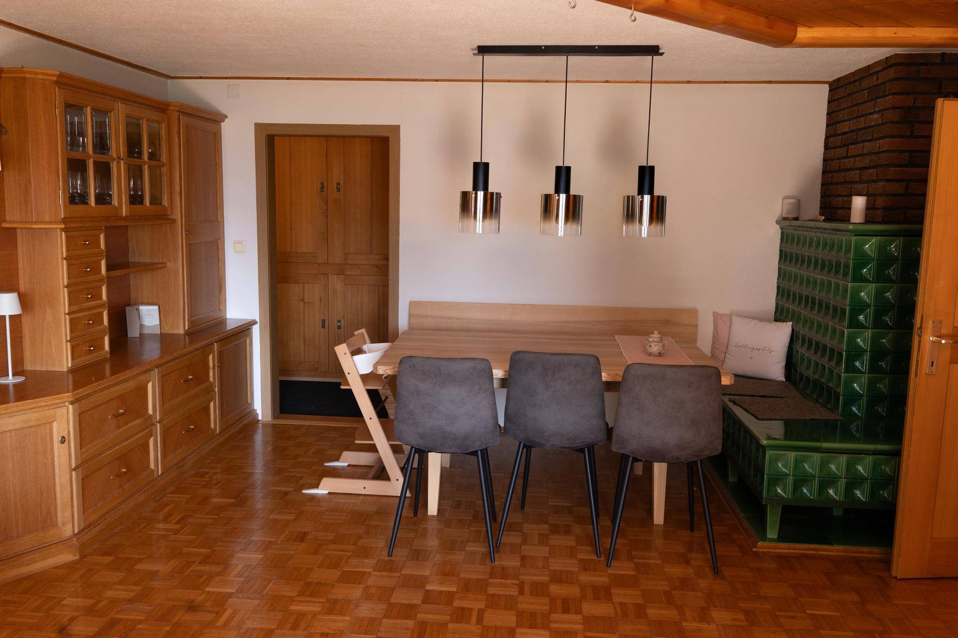 Traditioneller Essbereich mit Kachelofen, Holzbänken und passenden Möbeln in warmen Farbtönen.