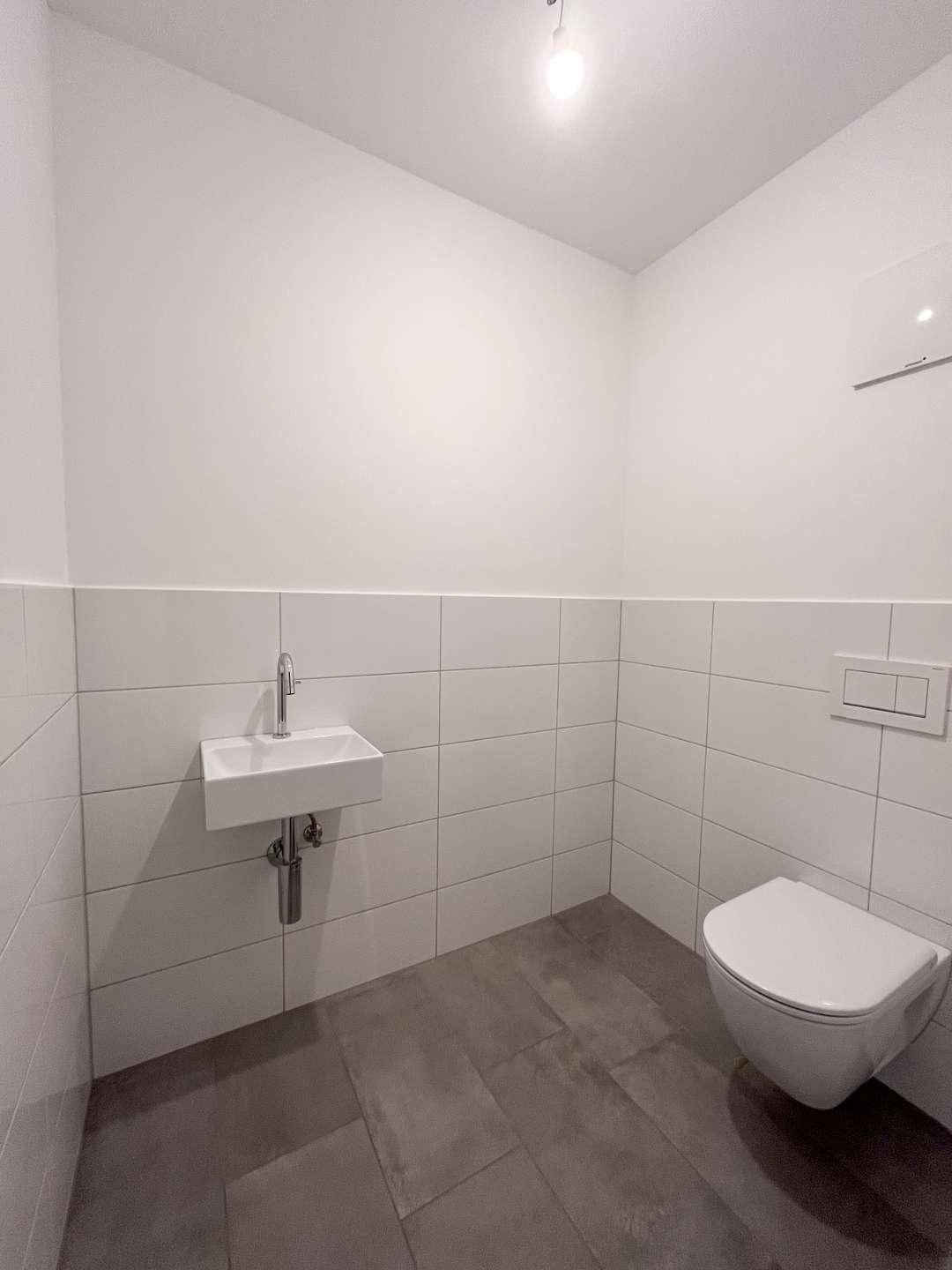 Kleines Gäste-WC mit weißen Wandfliesen, wandhängendem WC und modernem Waschbecken.