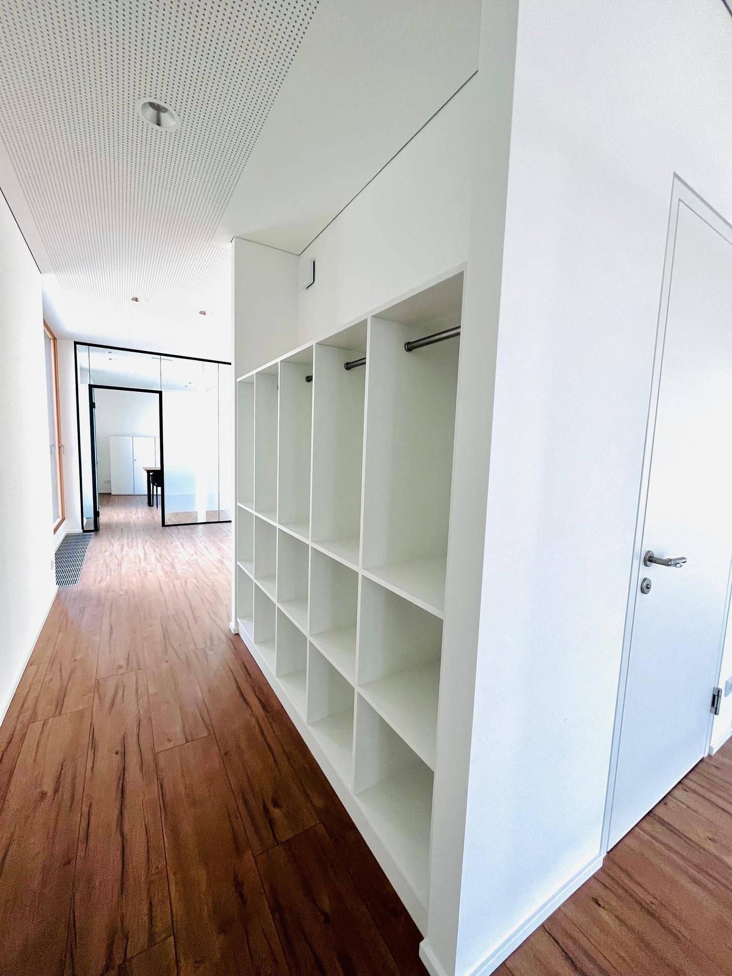 Heller Flur mit integrierten Regalen und Holzboden, der zu weiteren modernen Räumen führt.