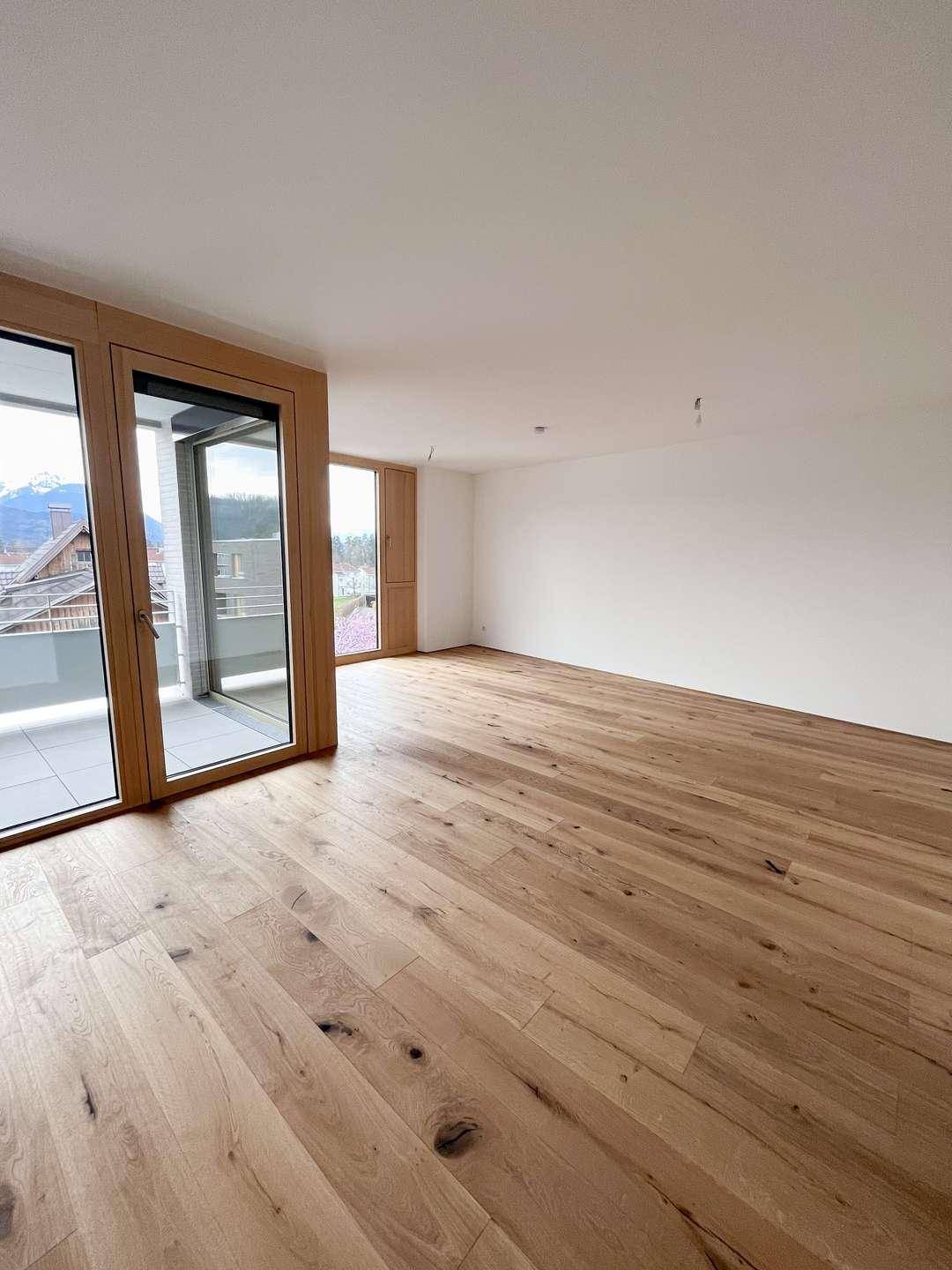 Heller, leerer Raum mit breiten Holzdielen und Zugang zu einem Balkon mit Bergblick.