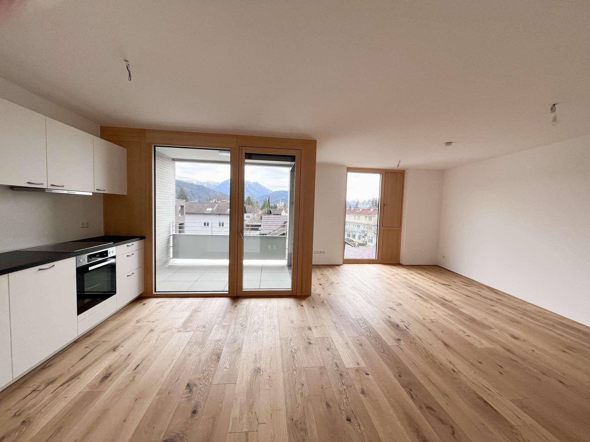 Offener Wohn- und Essbereich mit moderner Küche, Holzboden und großem Balkonzugang mit Bergblick.